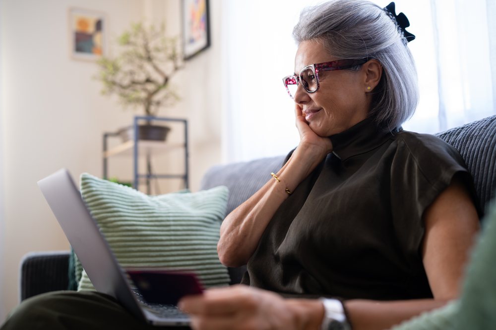 Mature white woman using laptop and credit card at home