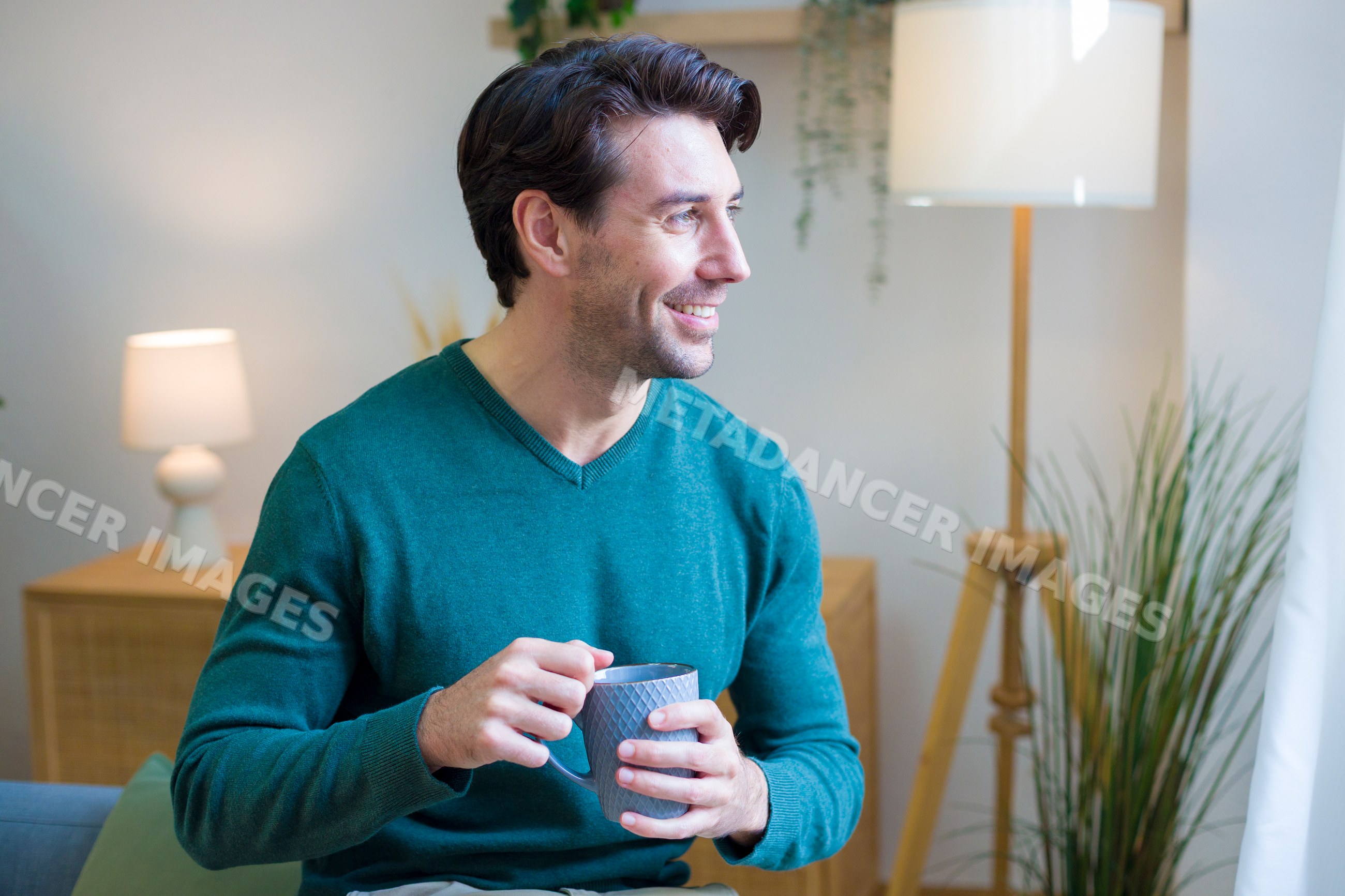 White man smiling and holding coffee cup sitting indoors