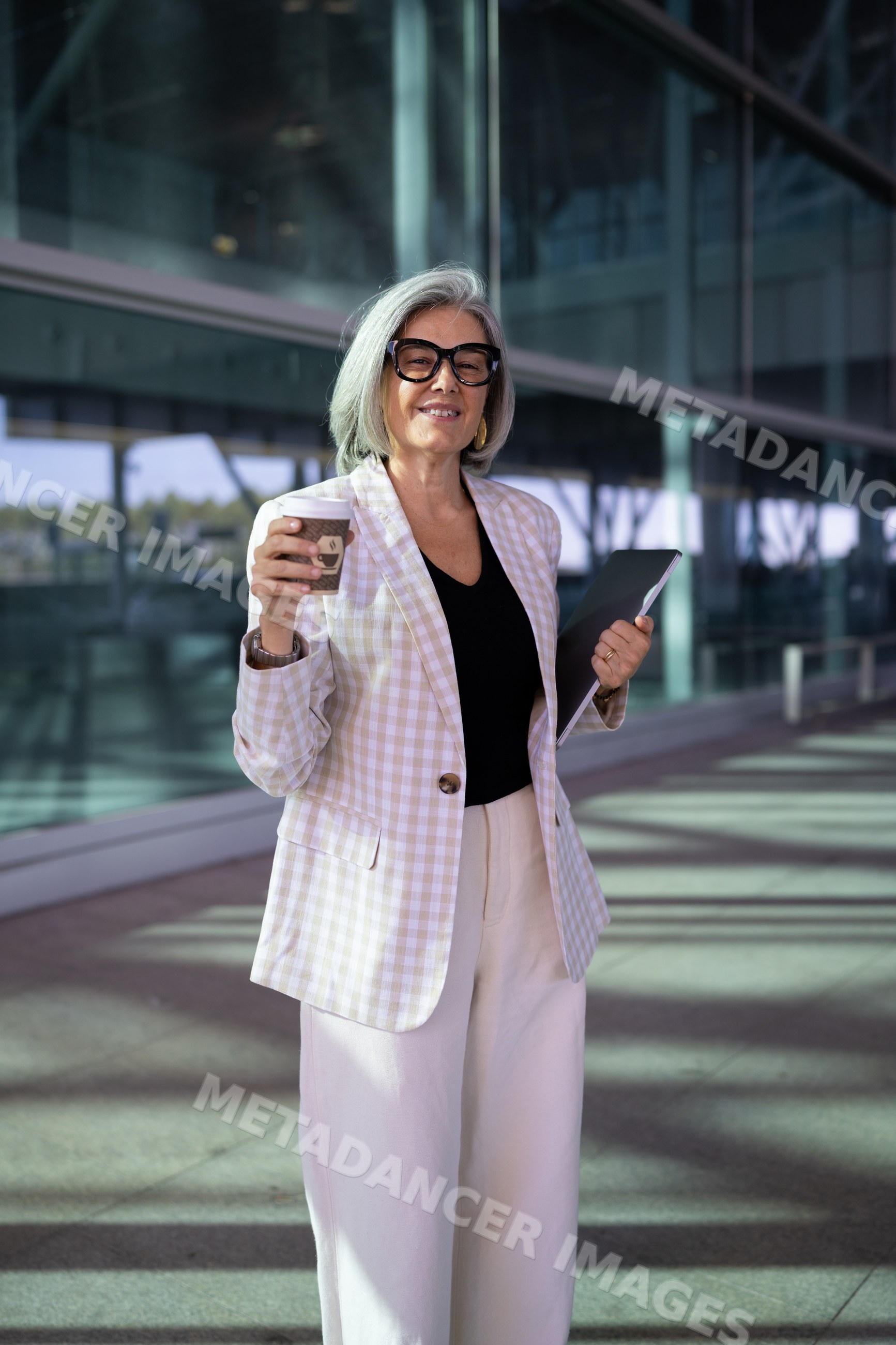 Businesswoman holding coffee cup and folder outside modern building