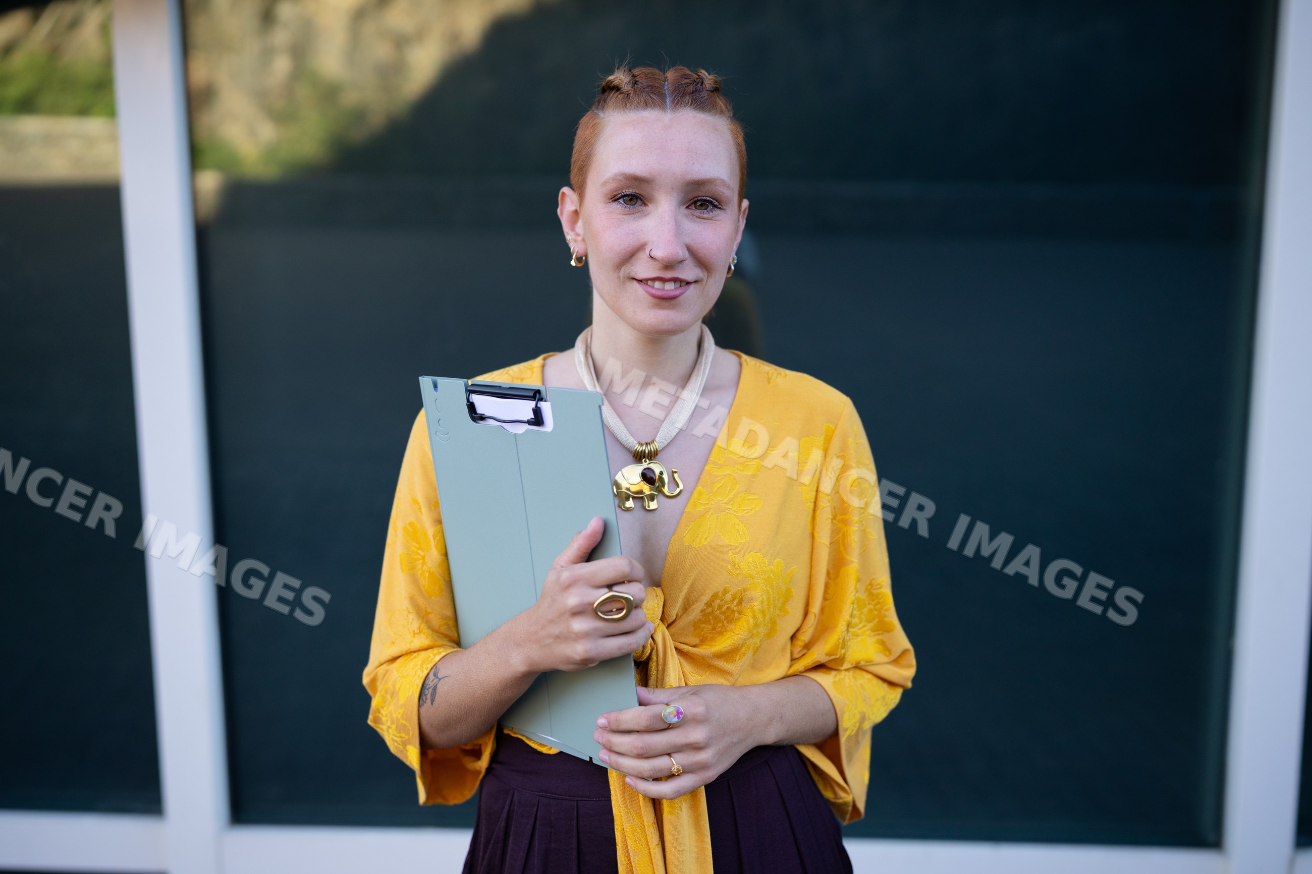 White woman holding clipboard wearing yellow top outdoors
