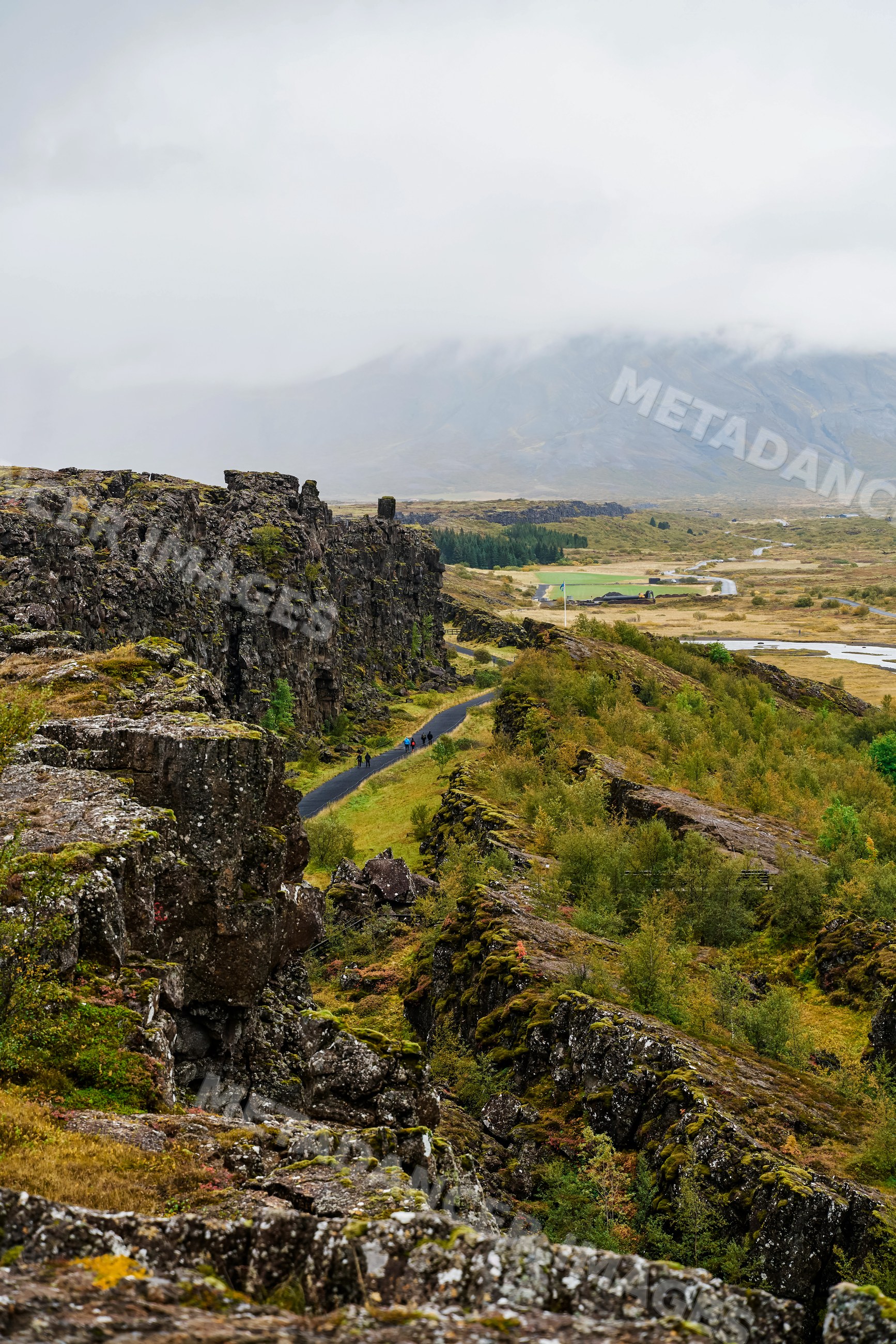 Hikers walk along volcanic rock cliffs on a misty trail