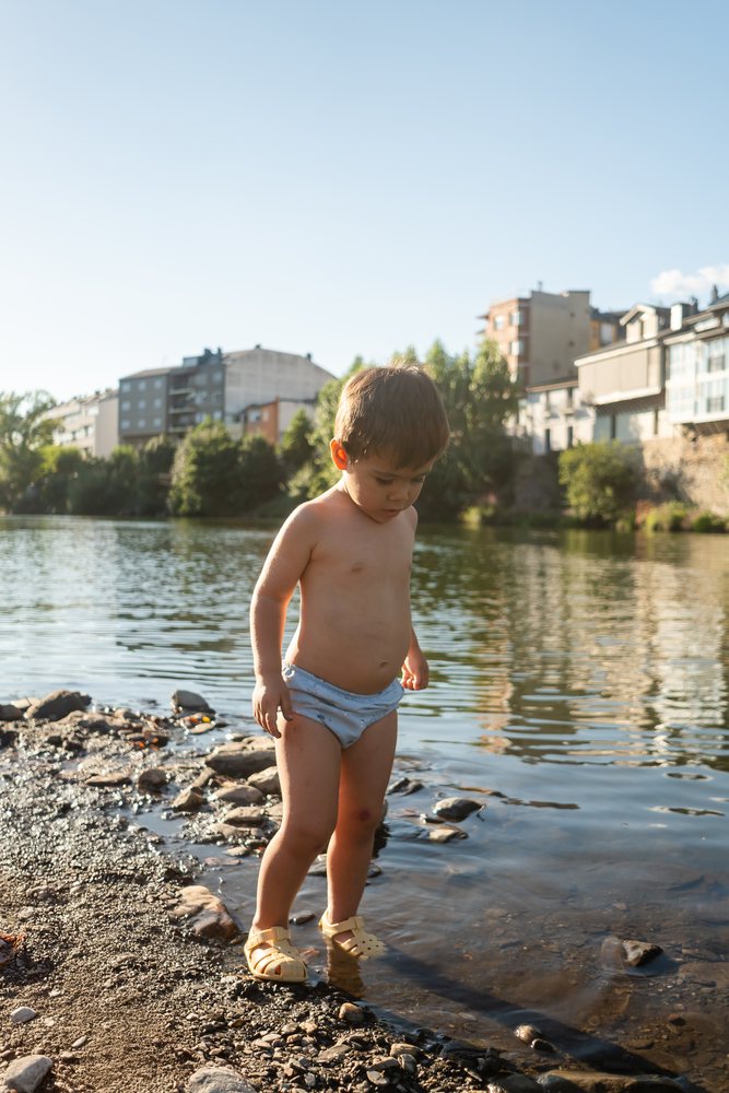 Toddler white boy exploring shallow riverbank water