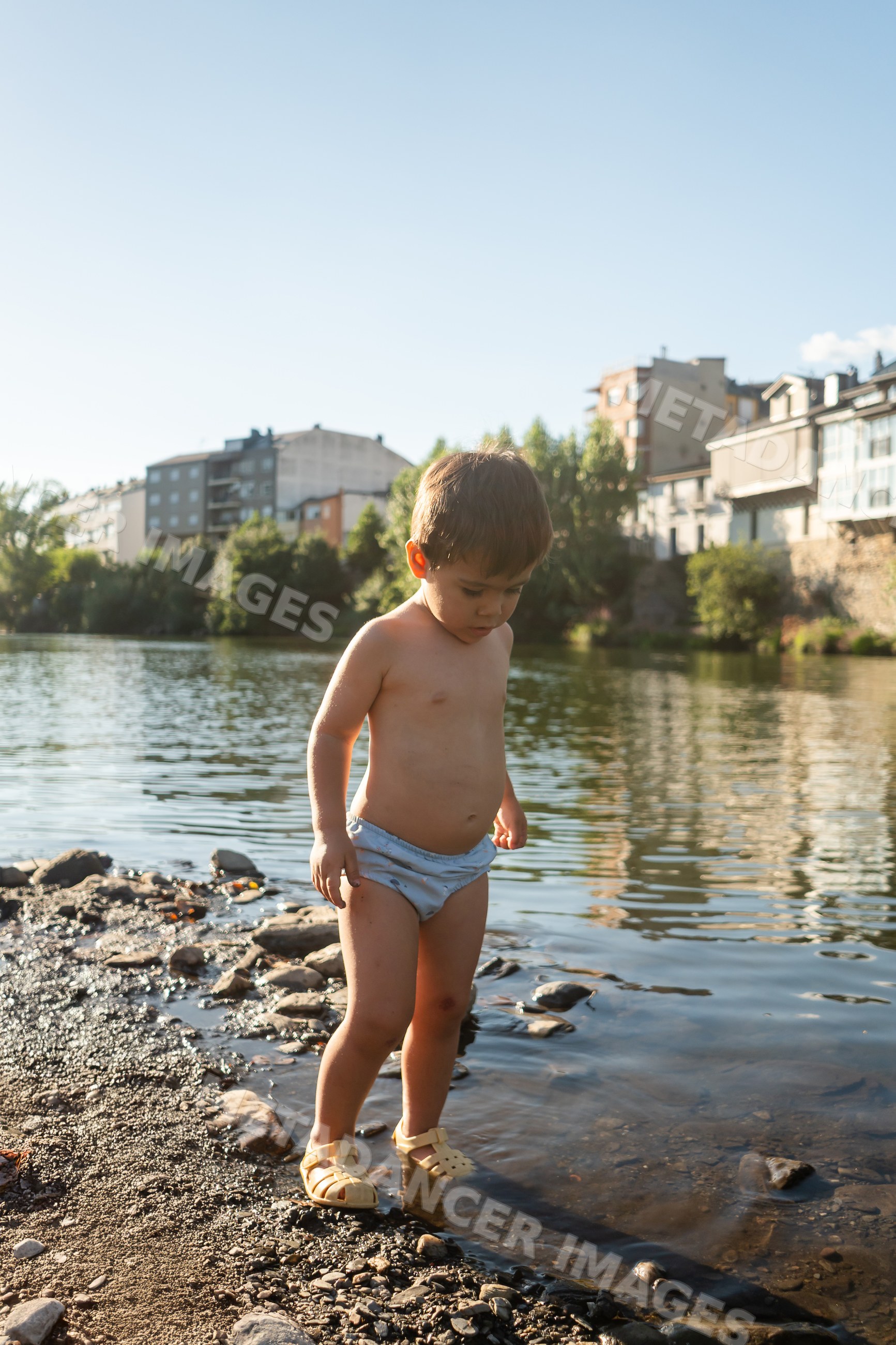 Toddler white boy exploring shallow riverbank water