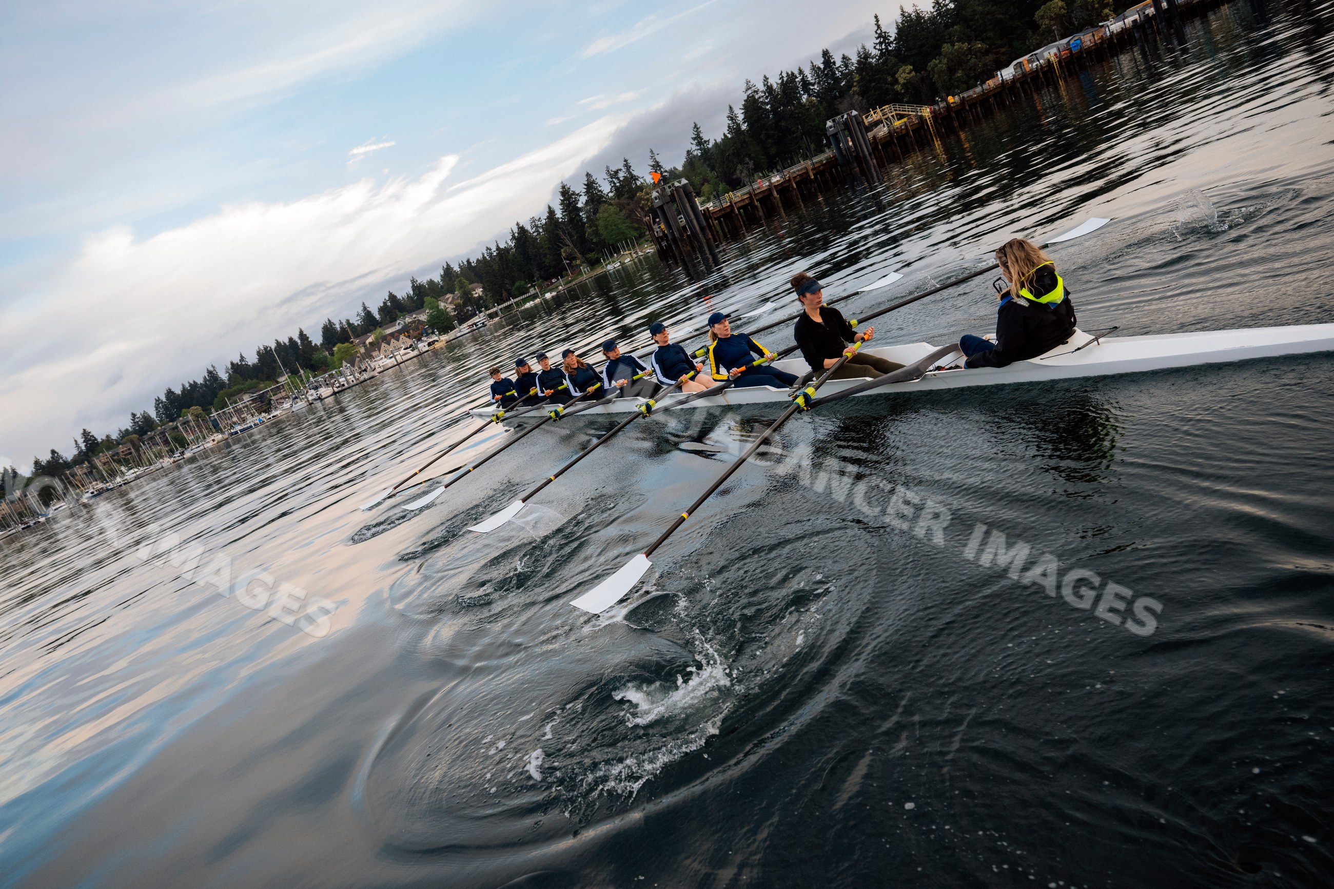 A white women's rowing team practicing rowing on calm coastal waters