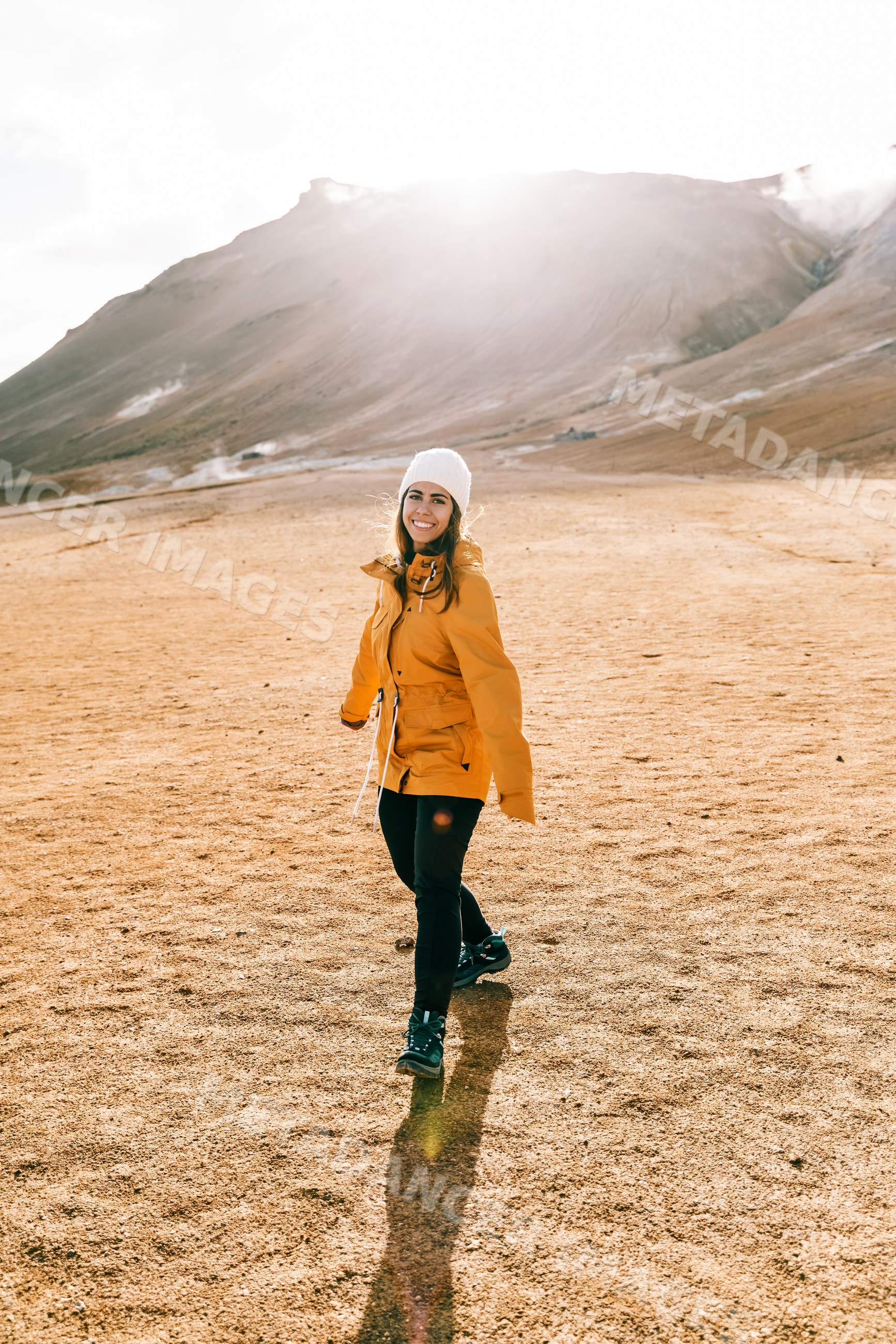 A white woman hiking in a yellow jacket enjoys a sunny mountain