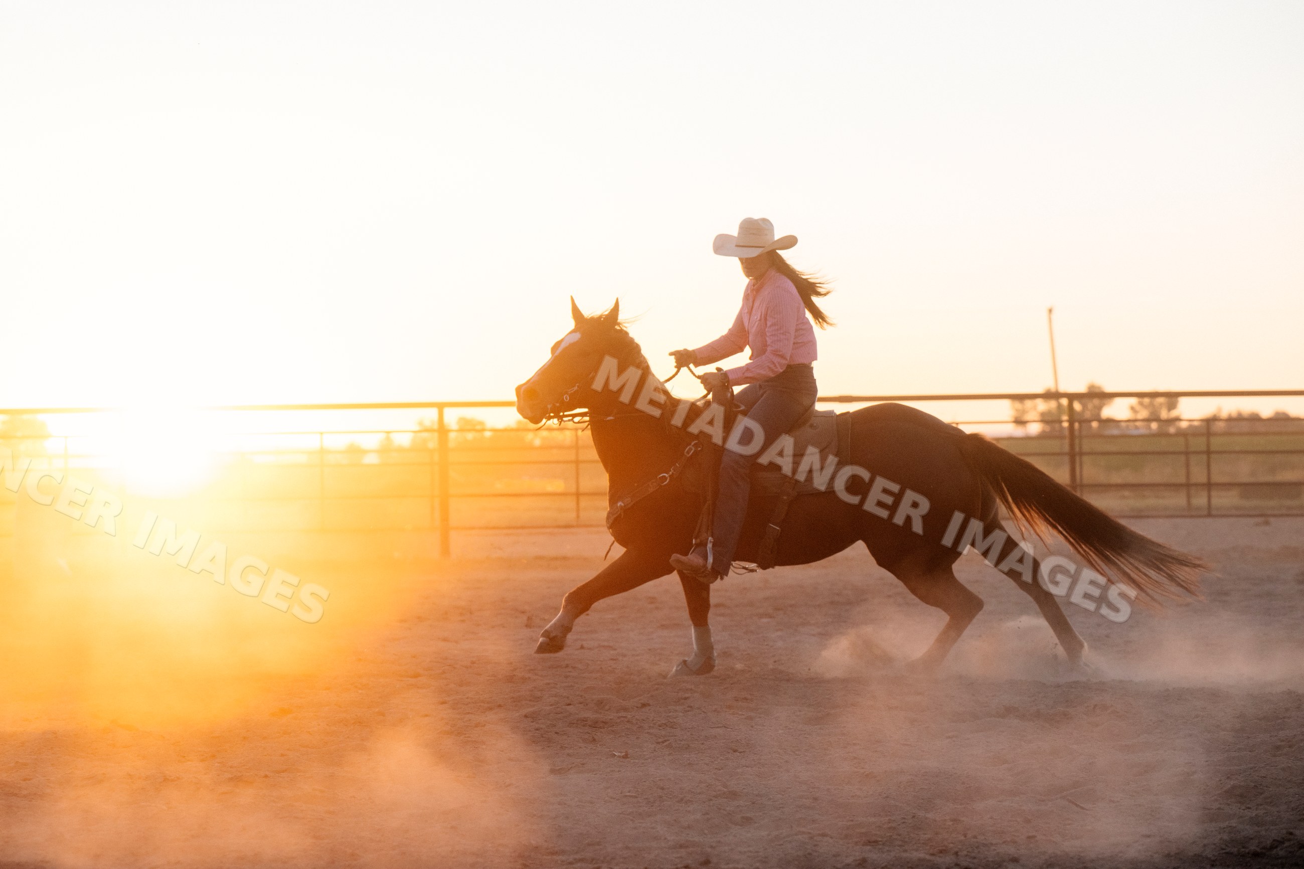 Horse rider in cowboy hat in dusty outdoor arena at sunset