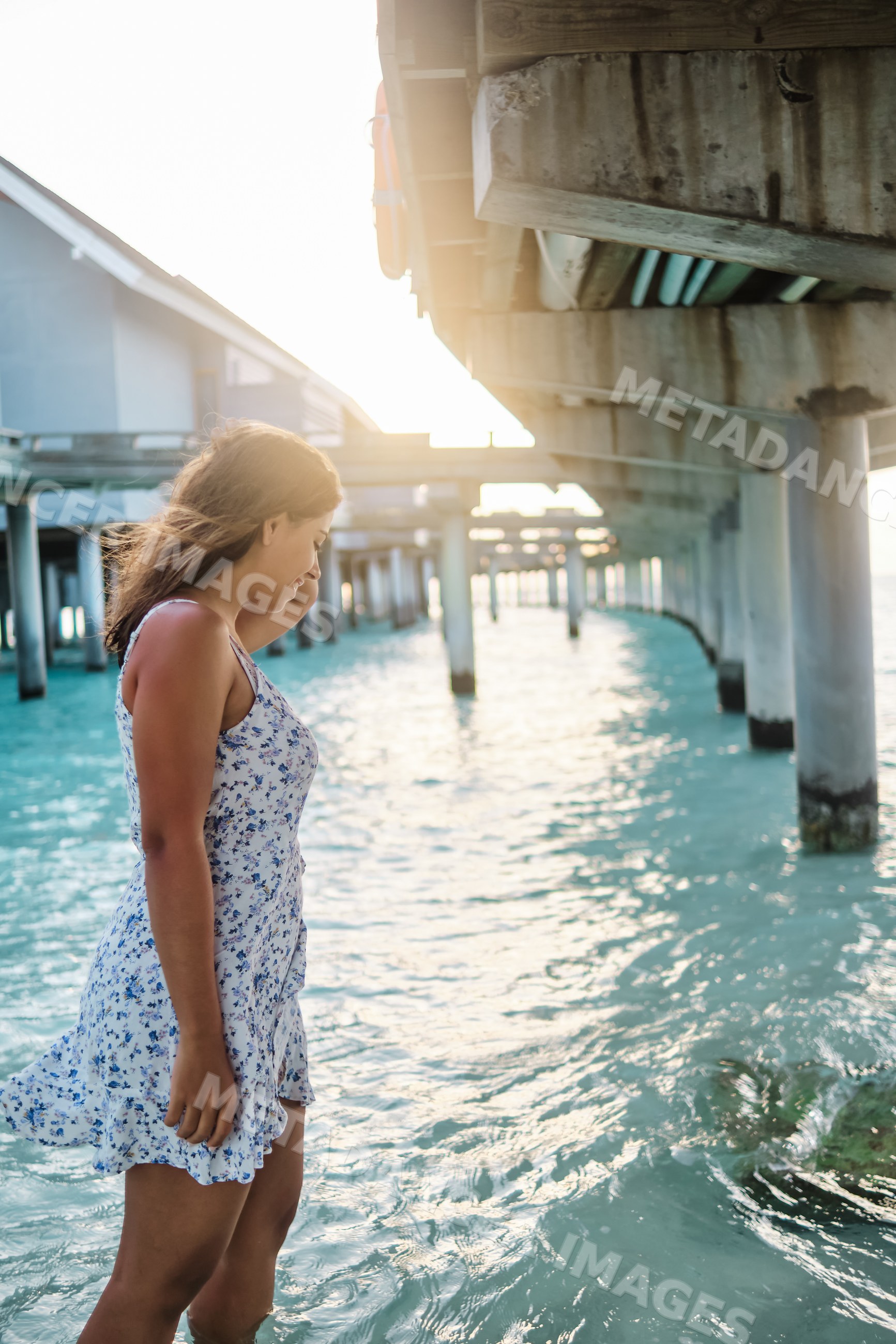 A young white woman walks in the ocean water under a pier
