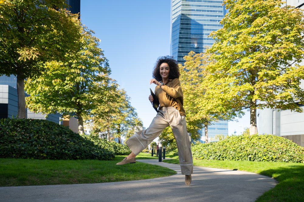 Woman jumping happily in Madrid urban park with trees and modern