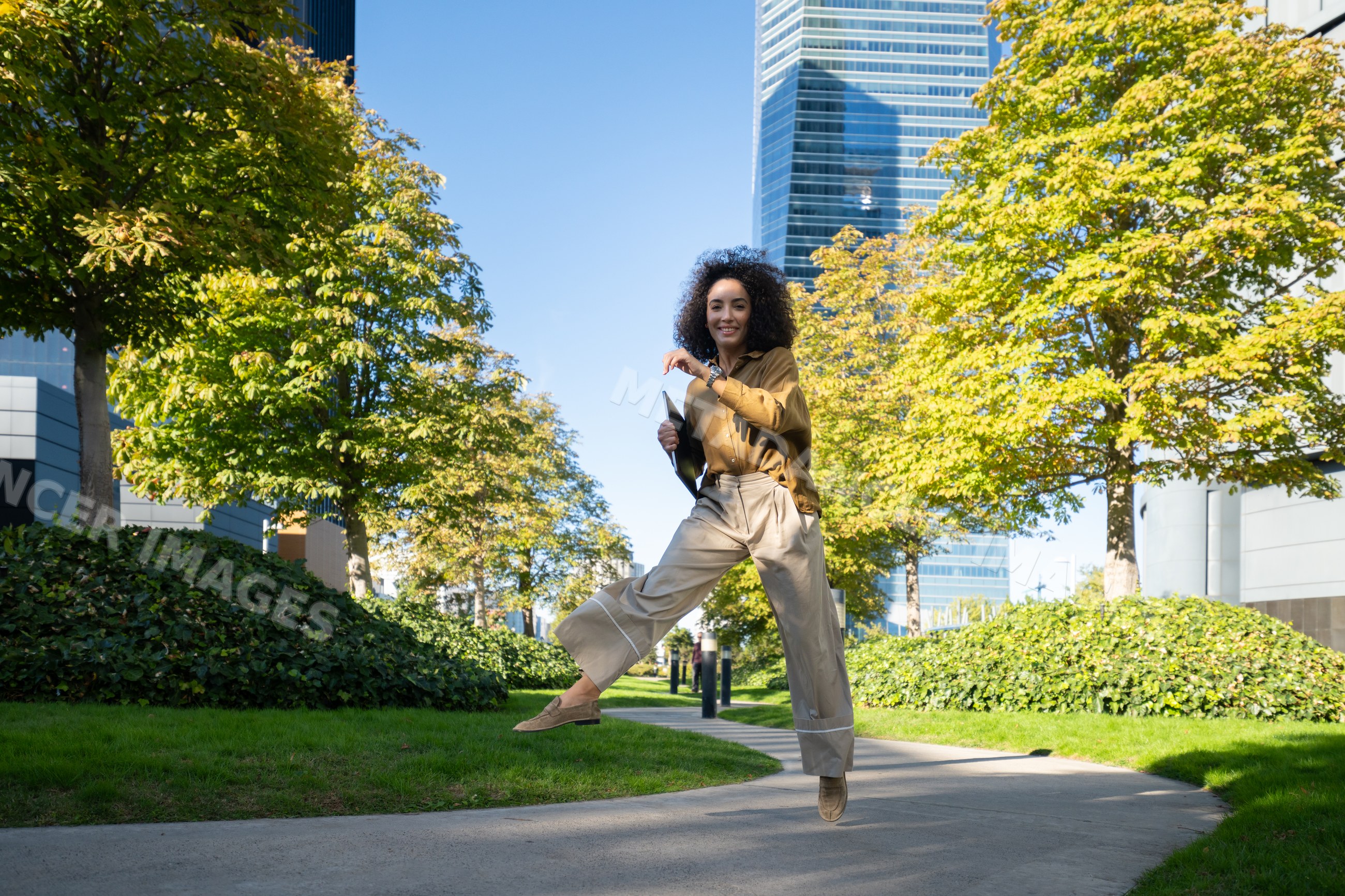 Woman jumping happily in Madrid urban park with trees and modern