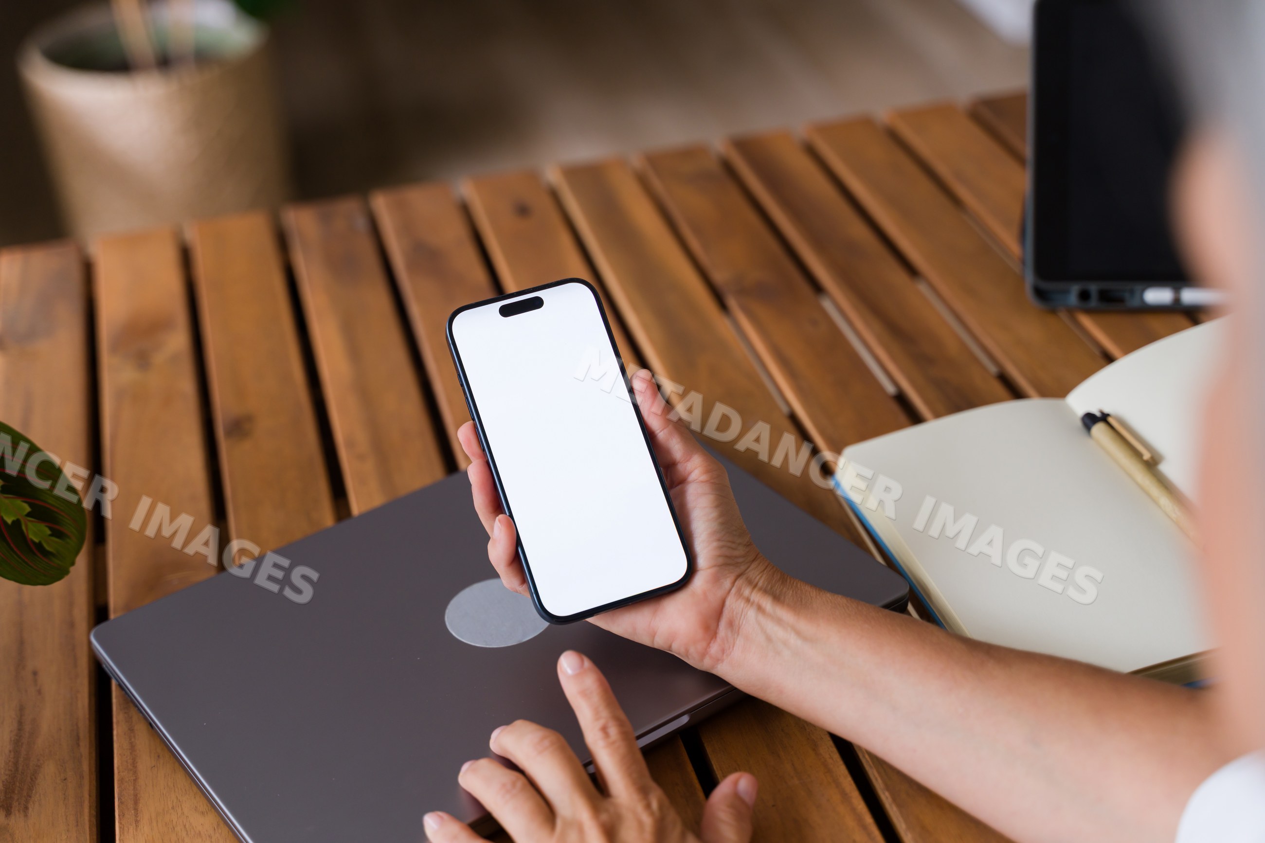 White Person holding smartphone with blank screen over wooden desk