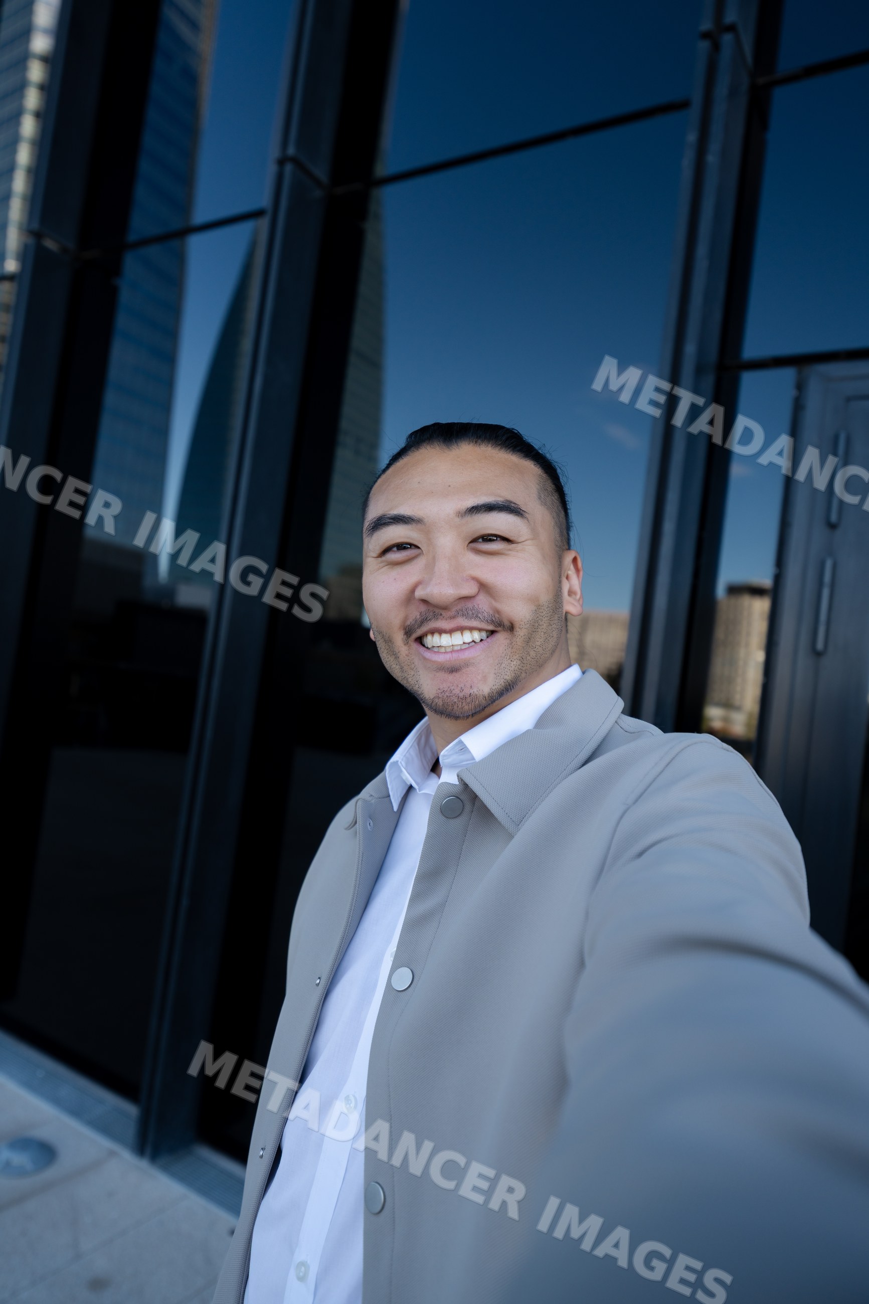 Man taking a smiling selfie outdoors by urban glass building
