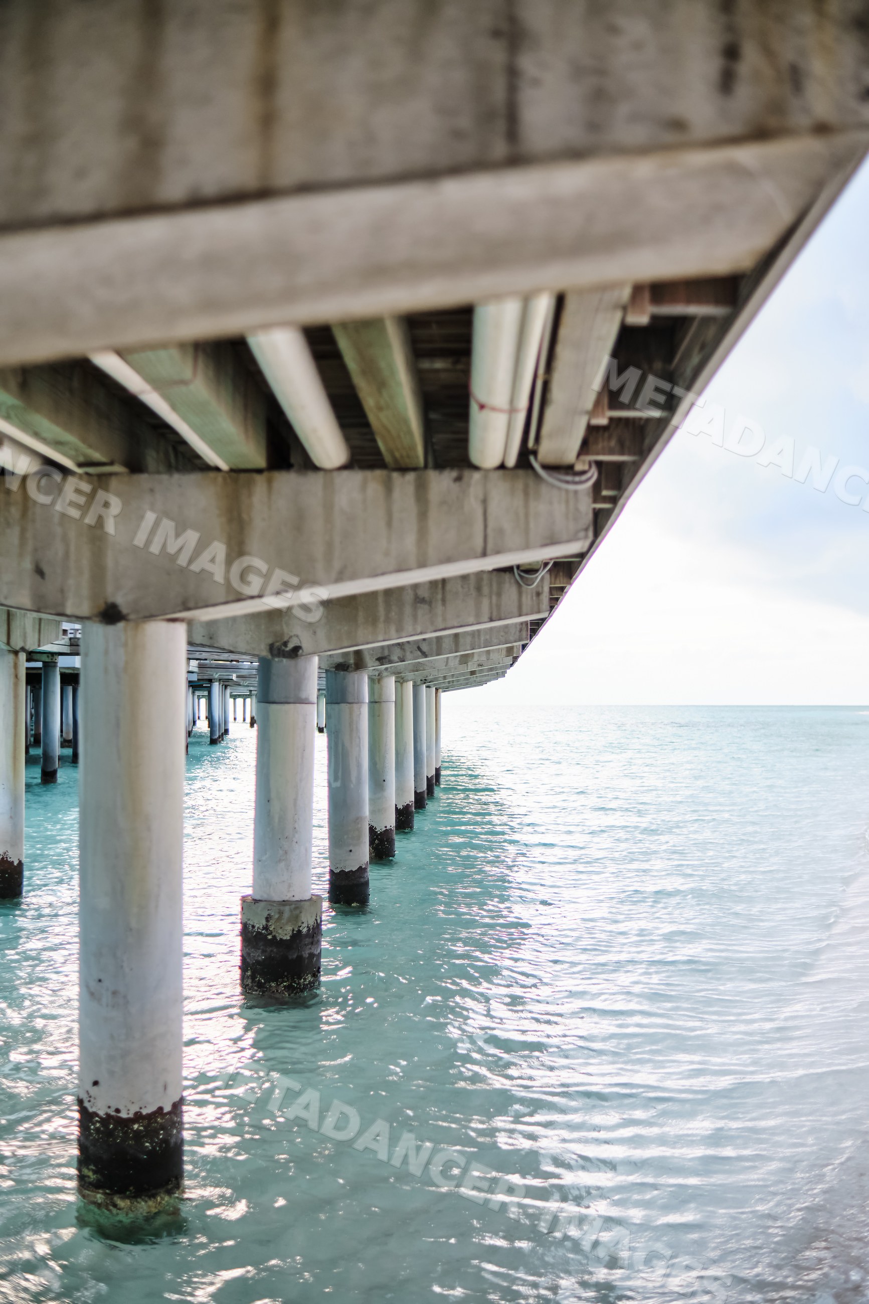 View underneath a concrete pier with pillars in turquoise ocean water