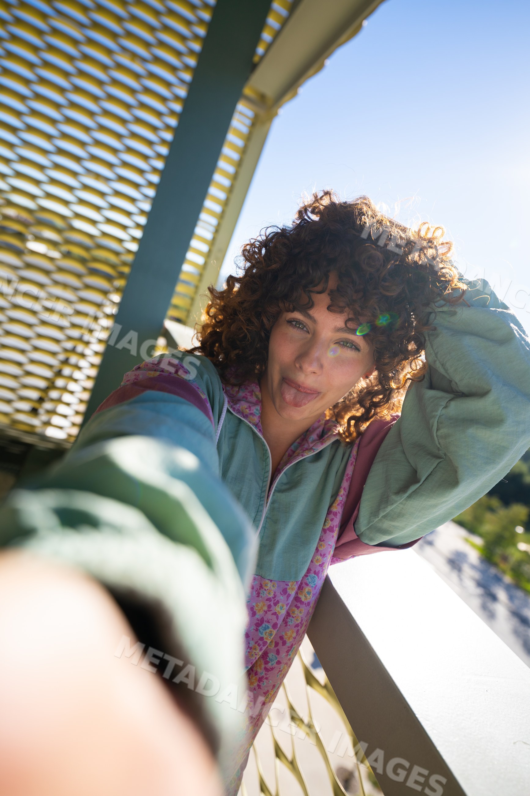 White woman with curly hair taking a playful selfie on sunny balcony