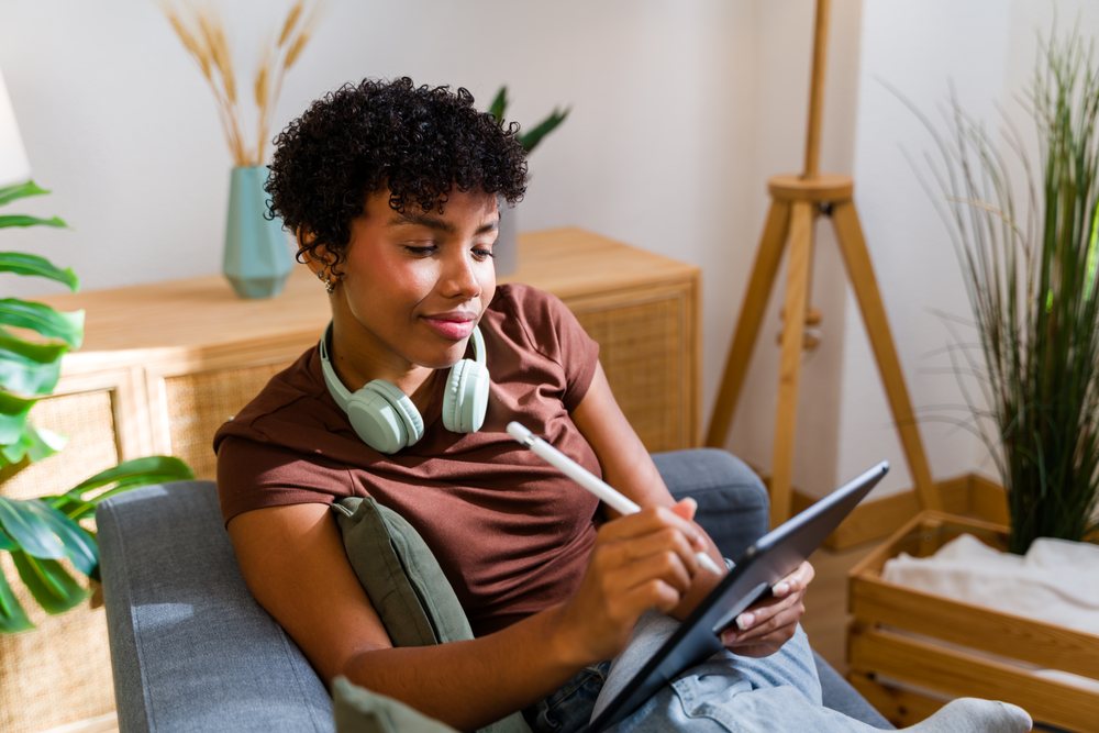 African American woman using tablet with stylus pen on couch