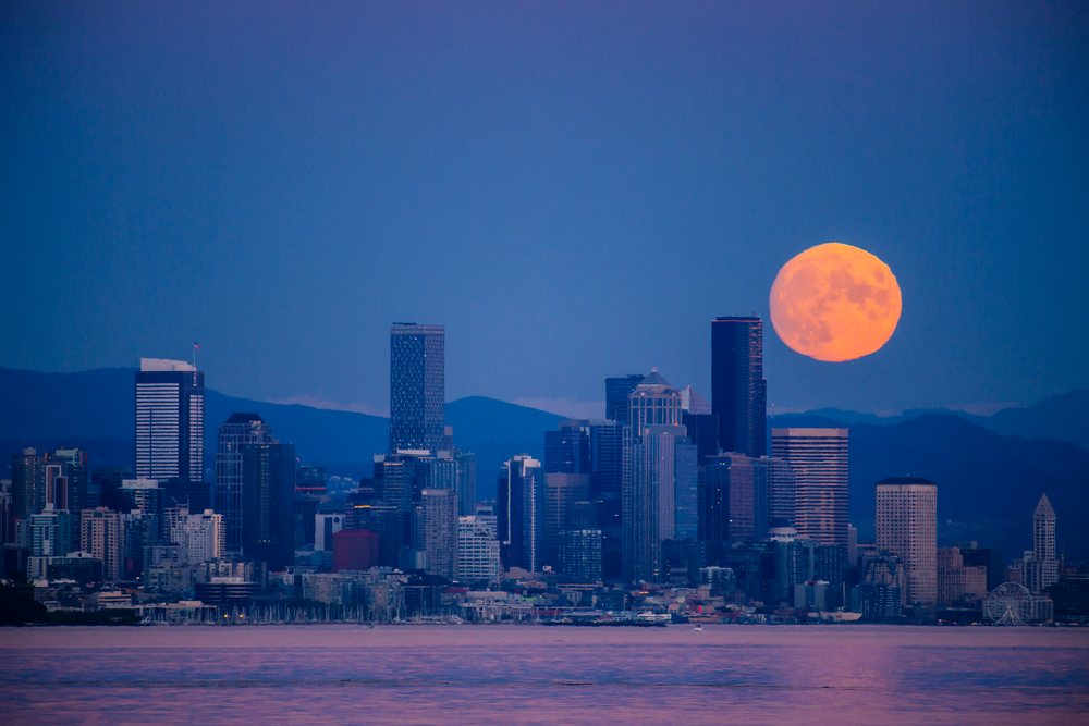 Full moon rising over Seattle downtown skyline with waterfront at dusk