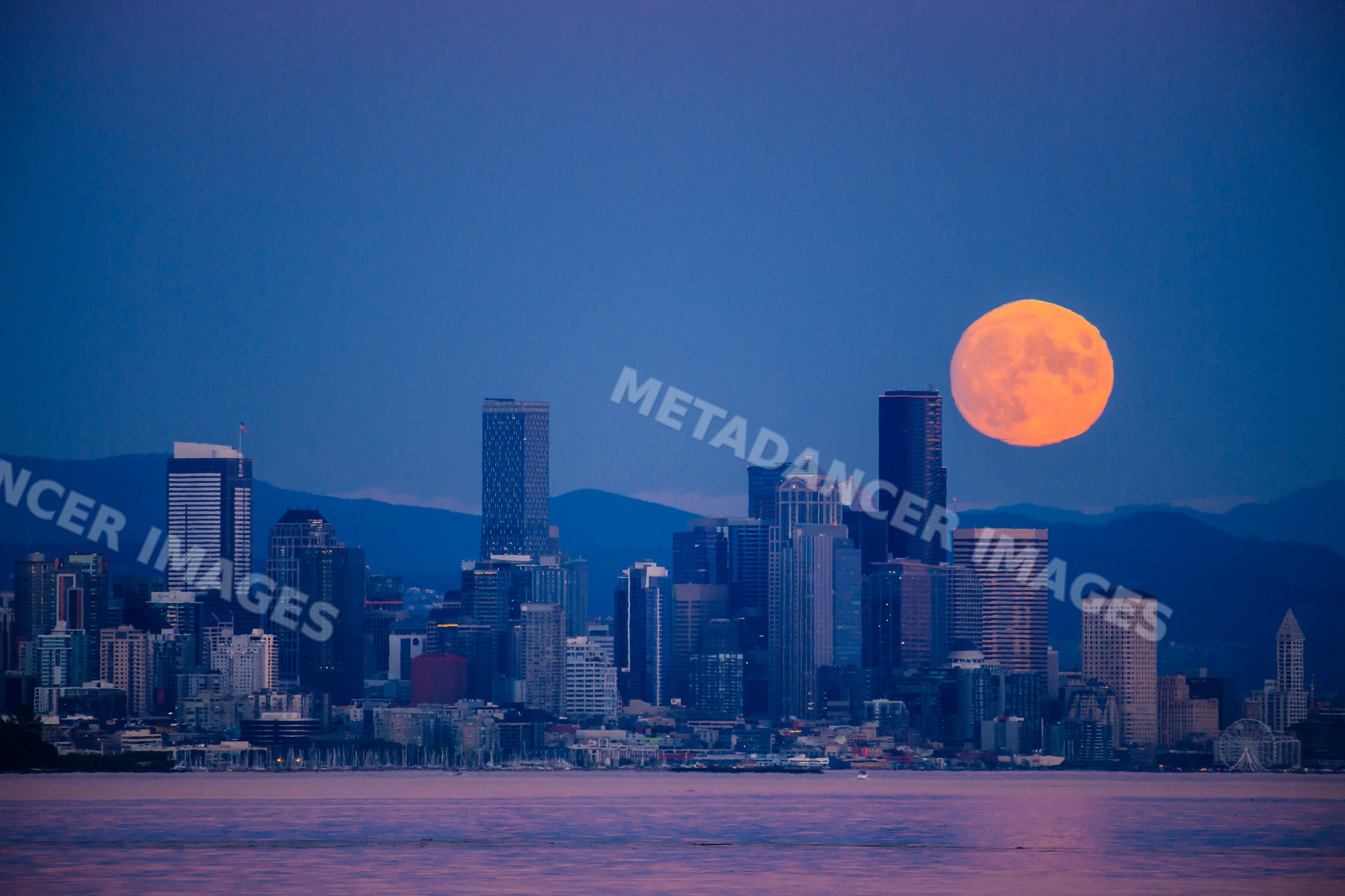 Full moon rising over Seattle downtown skyline with waterfront at dusk