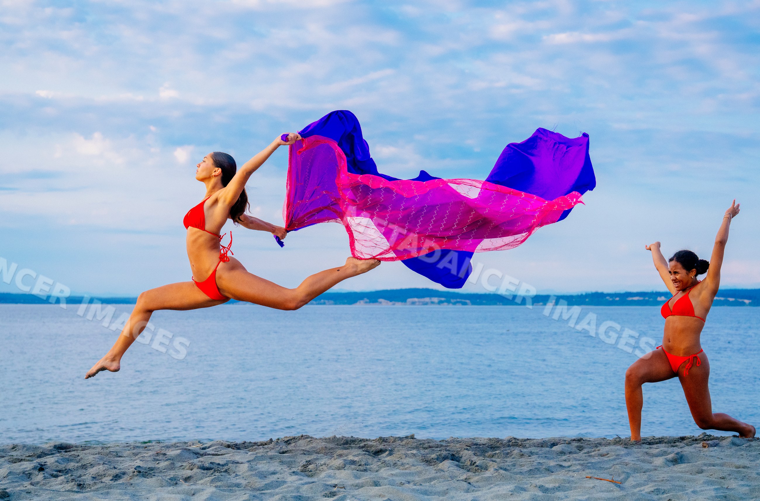 Two women performing partner acrobatics with a scarf on a beach