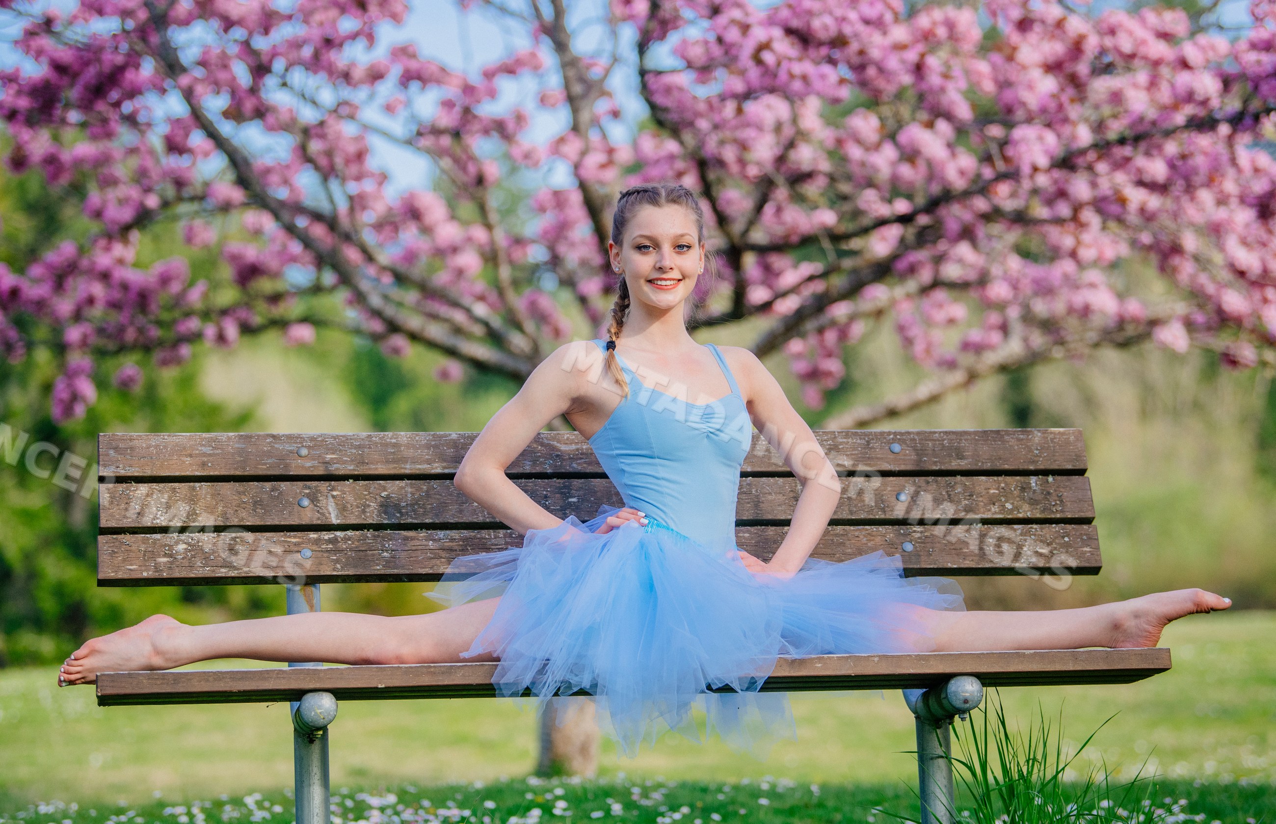 Ballet white dancer performing split on bench outdoors with flowering