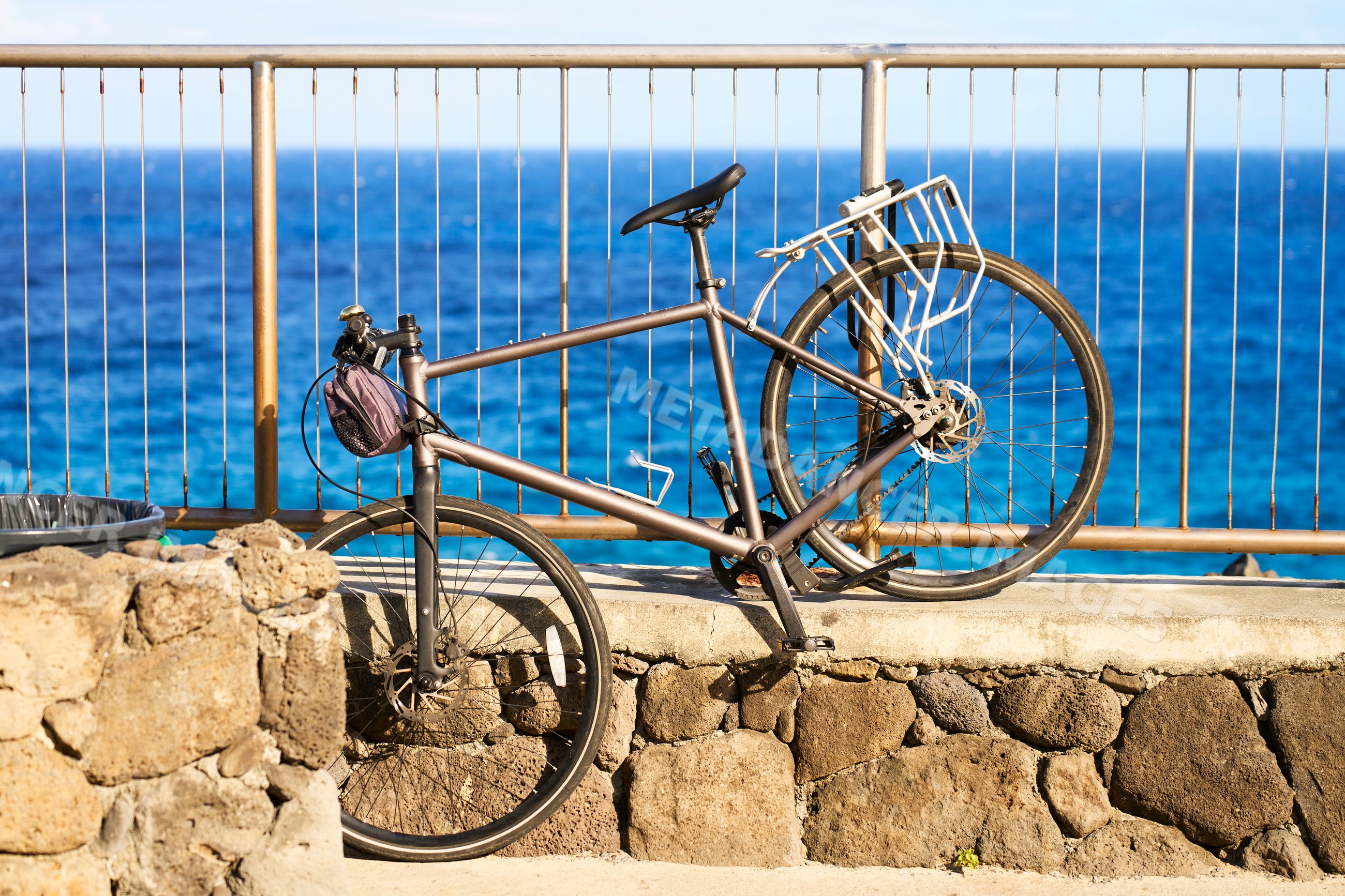 Bicycle resting against metal railing and stone wall along ocean