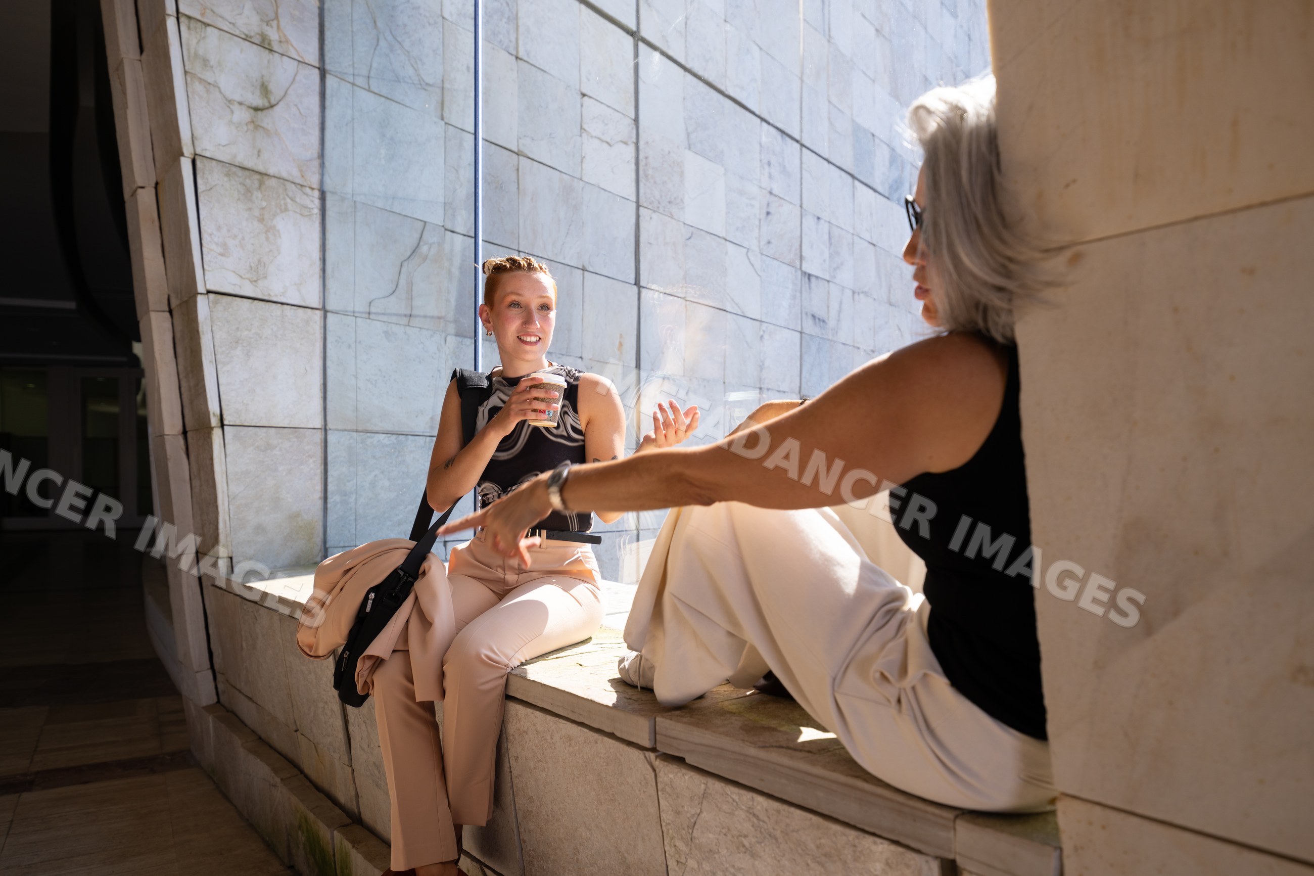 Two white women sitting and talking with coffee by window ledge