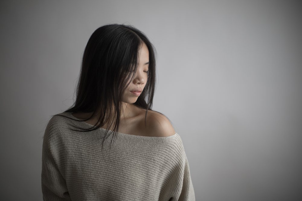 Southeast Asian woman in knitted off-shoulder sweater with serene