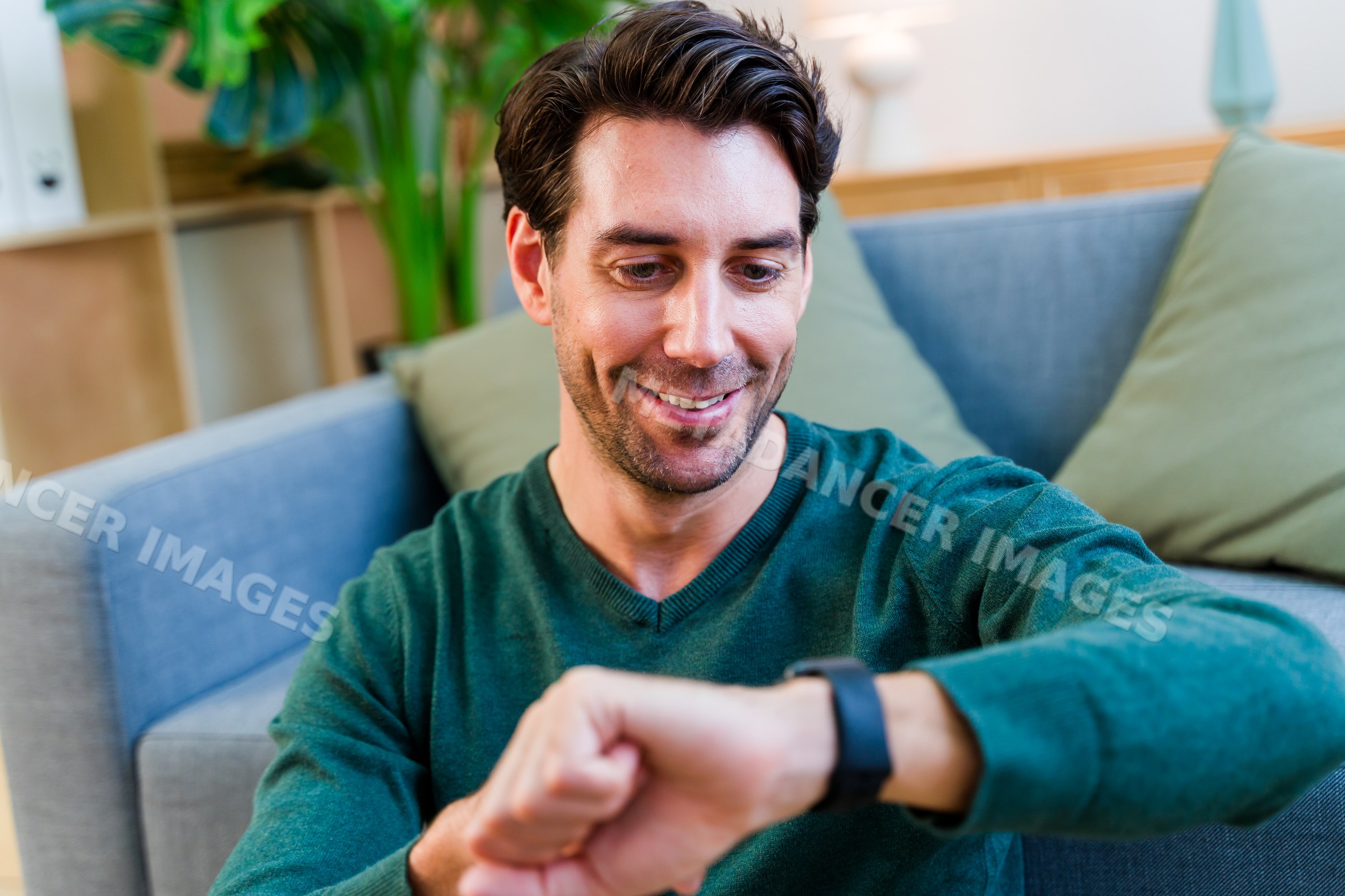 White man smiling and checking smartwatch in living room
