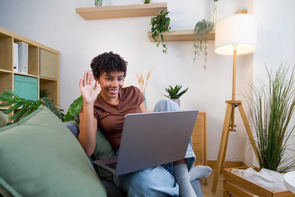 Young African American woman waving during video call on sofa at home