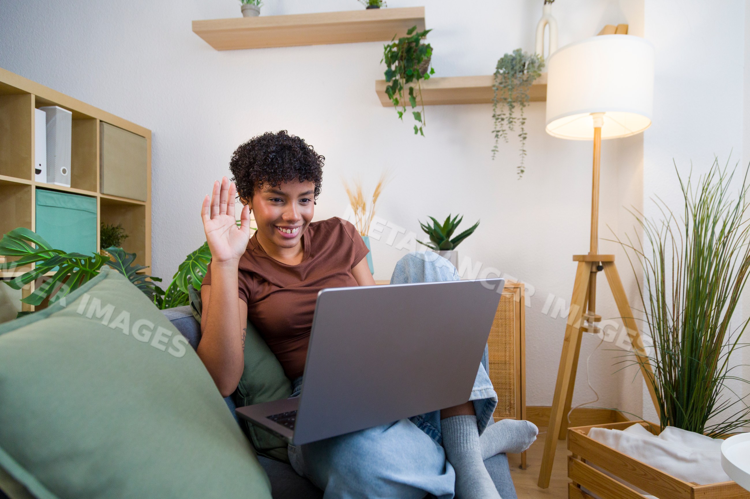 Young African American woman waving during video call on sofa at home