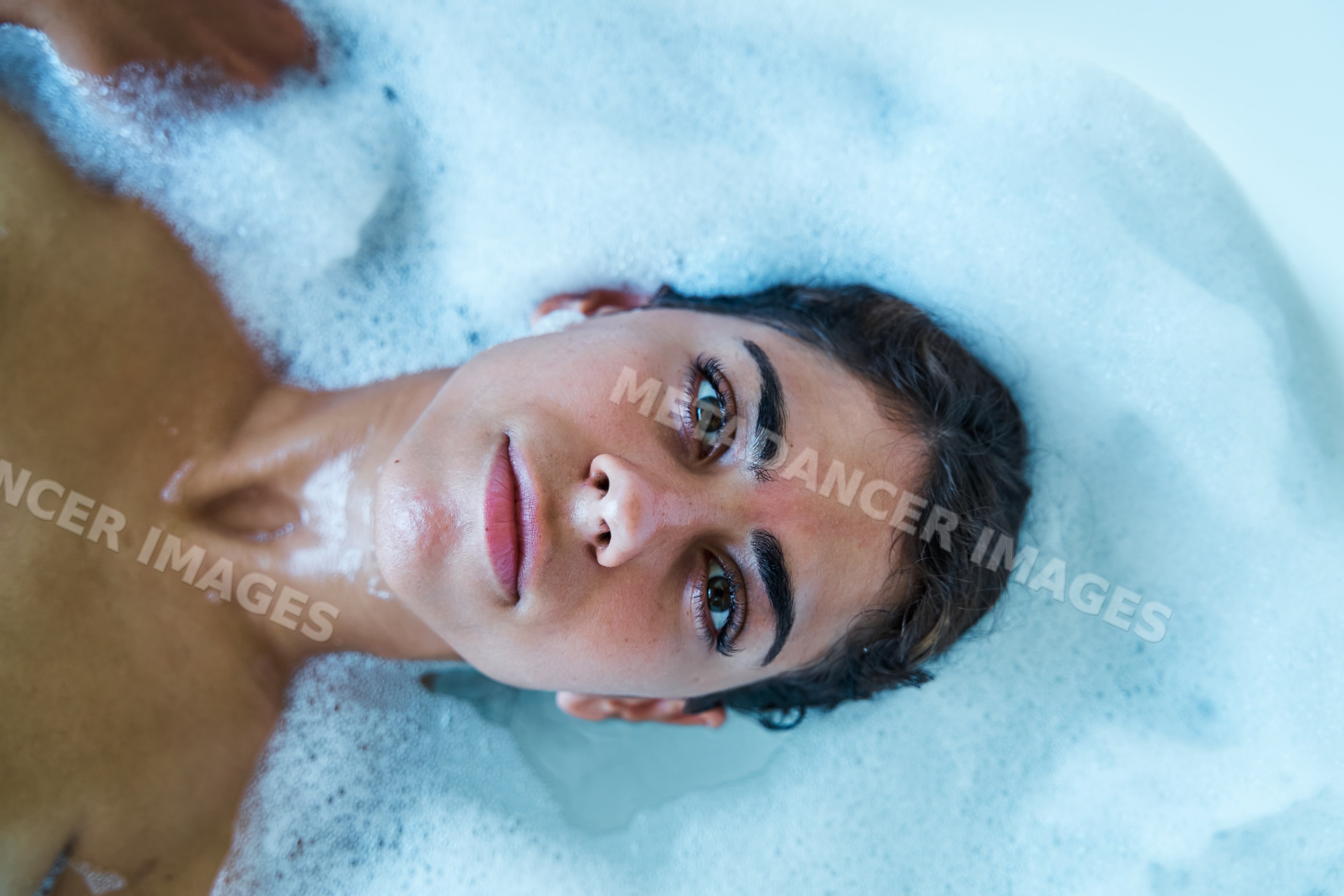 A white woman relaxes in a bubble bath with foam water