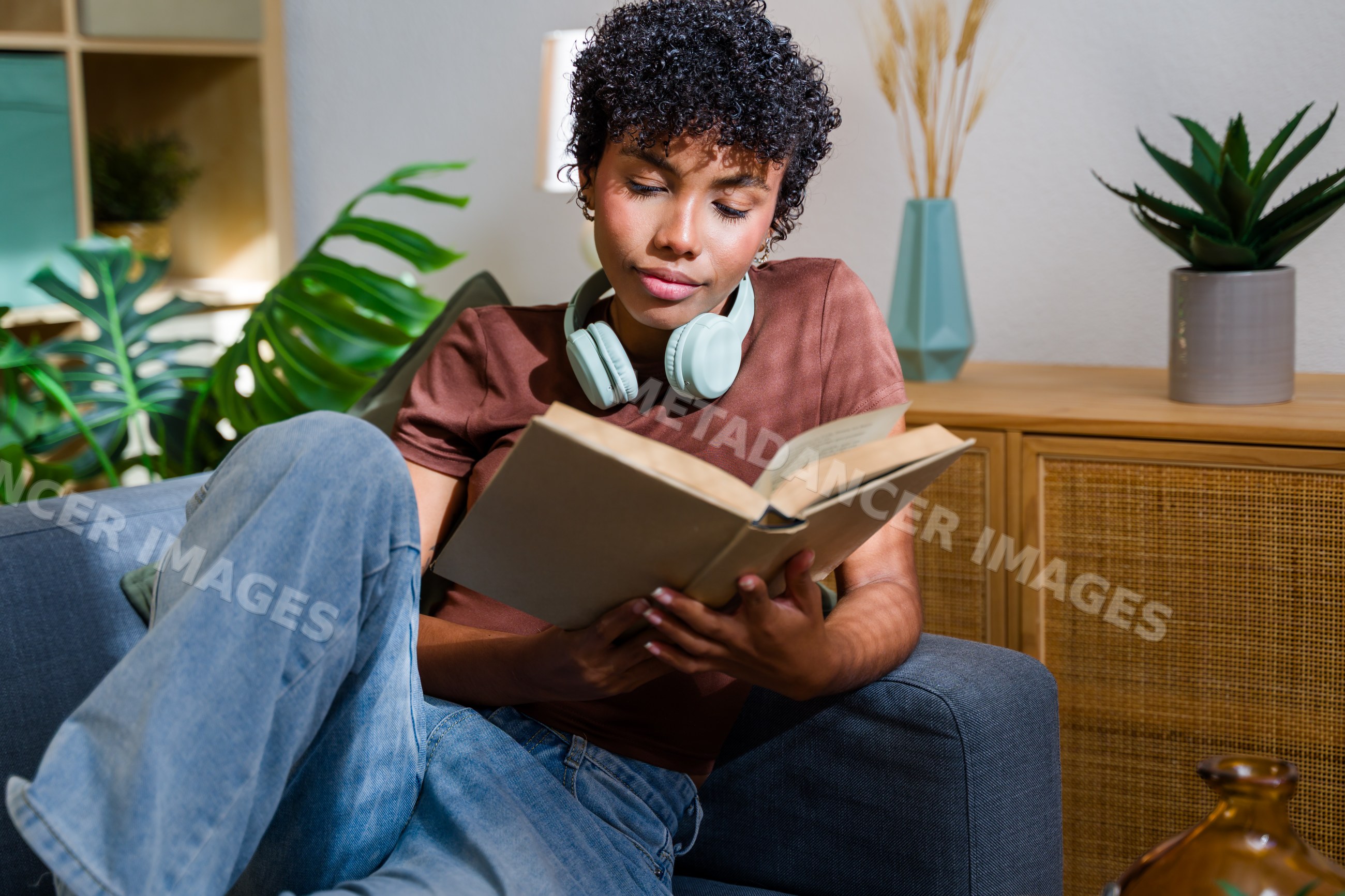African American woman reading book on sofa with headphones