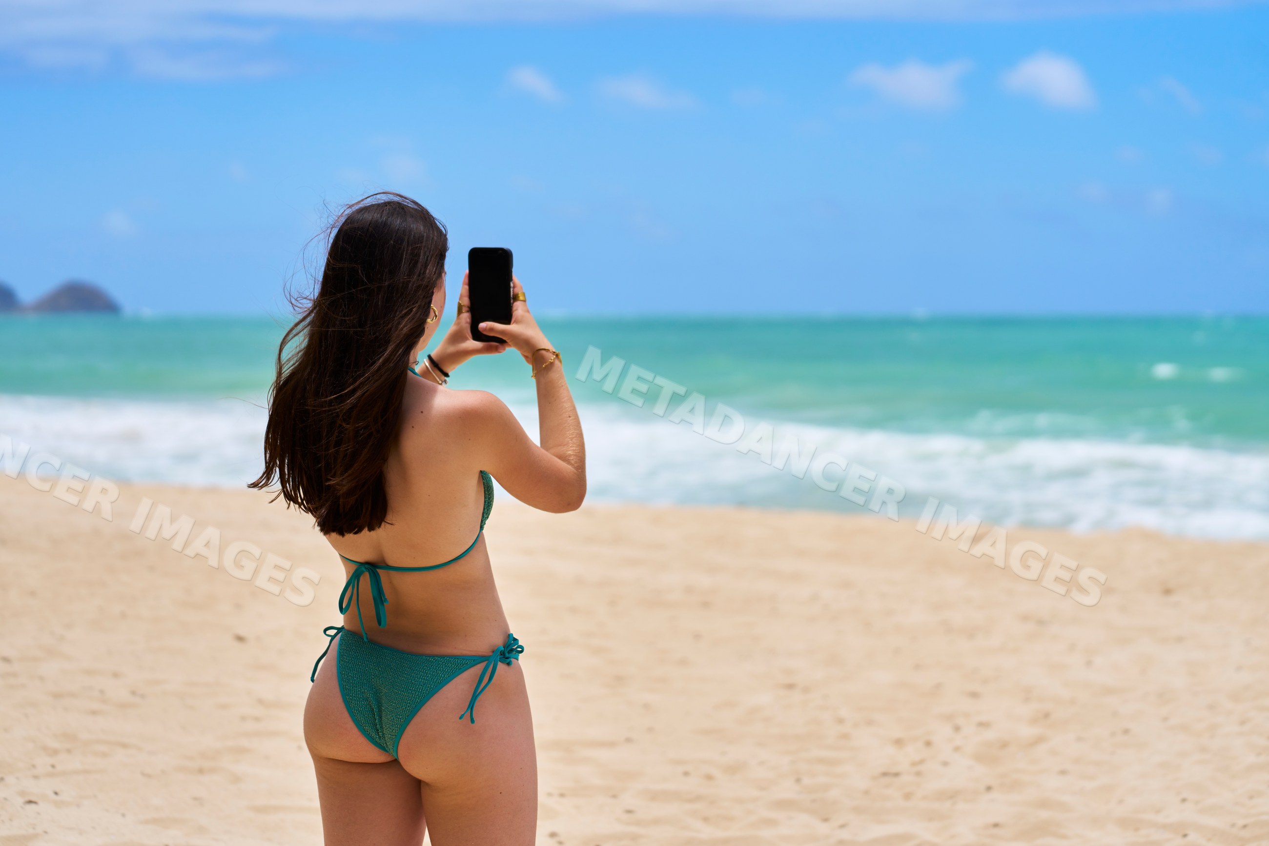 White woman taking photo on sandy Hawaii beach by the ocean