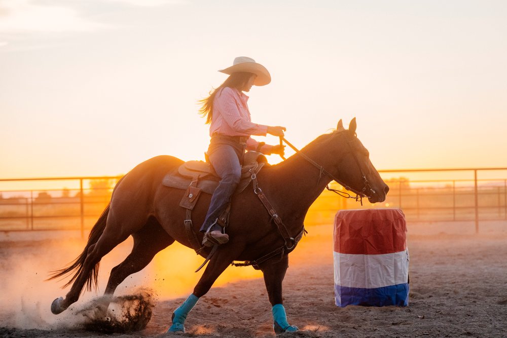 White woman riding horse at sunset during barrel racing