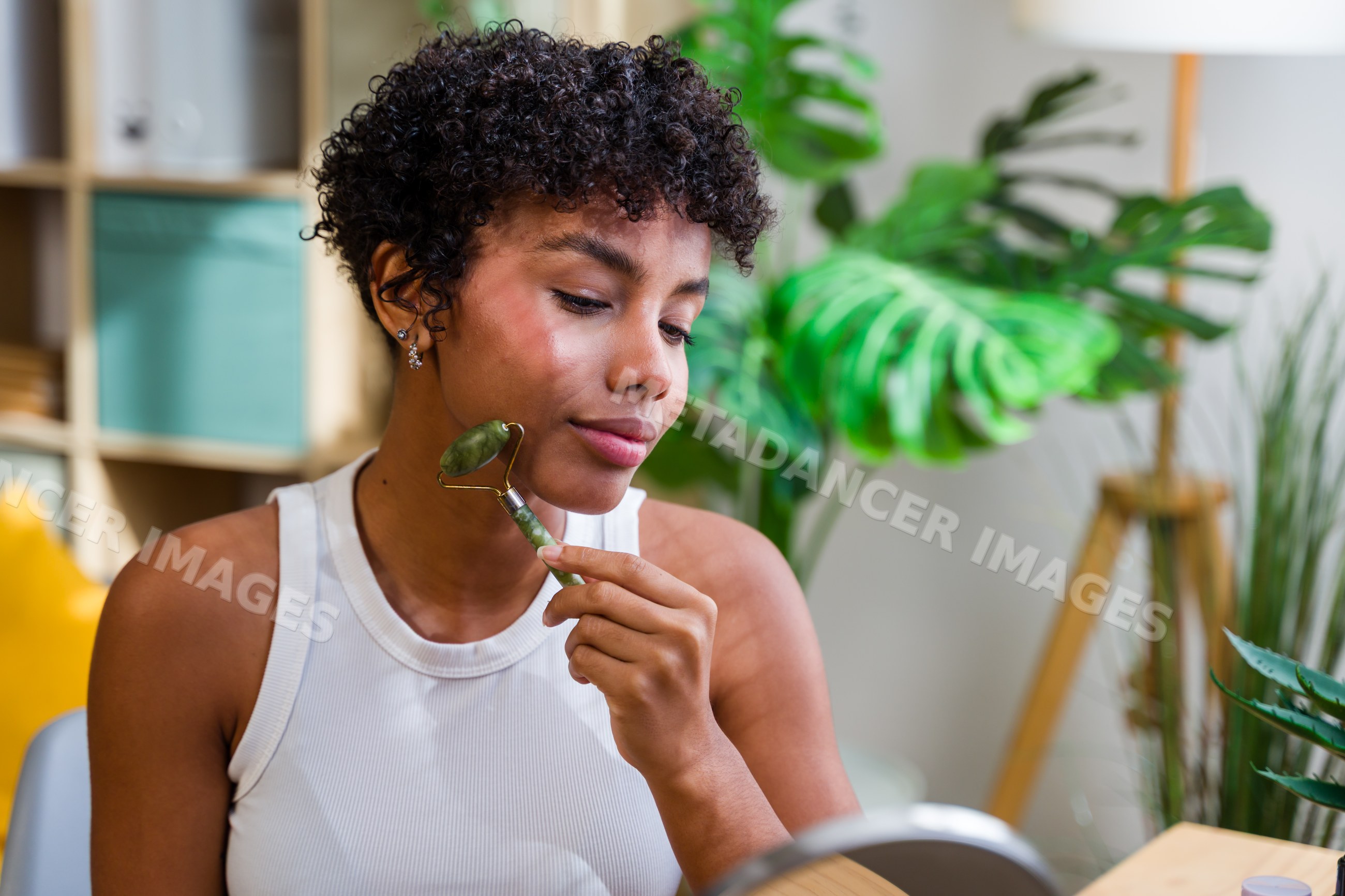 African American woman massaging face with jade roller indoors