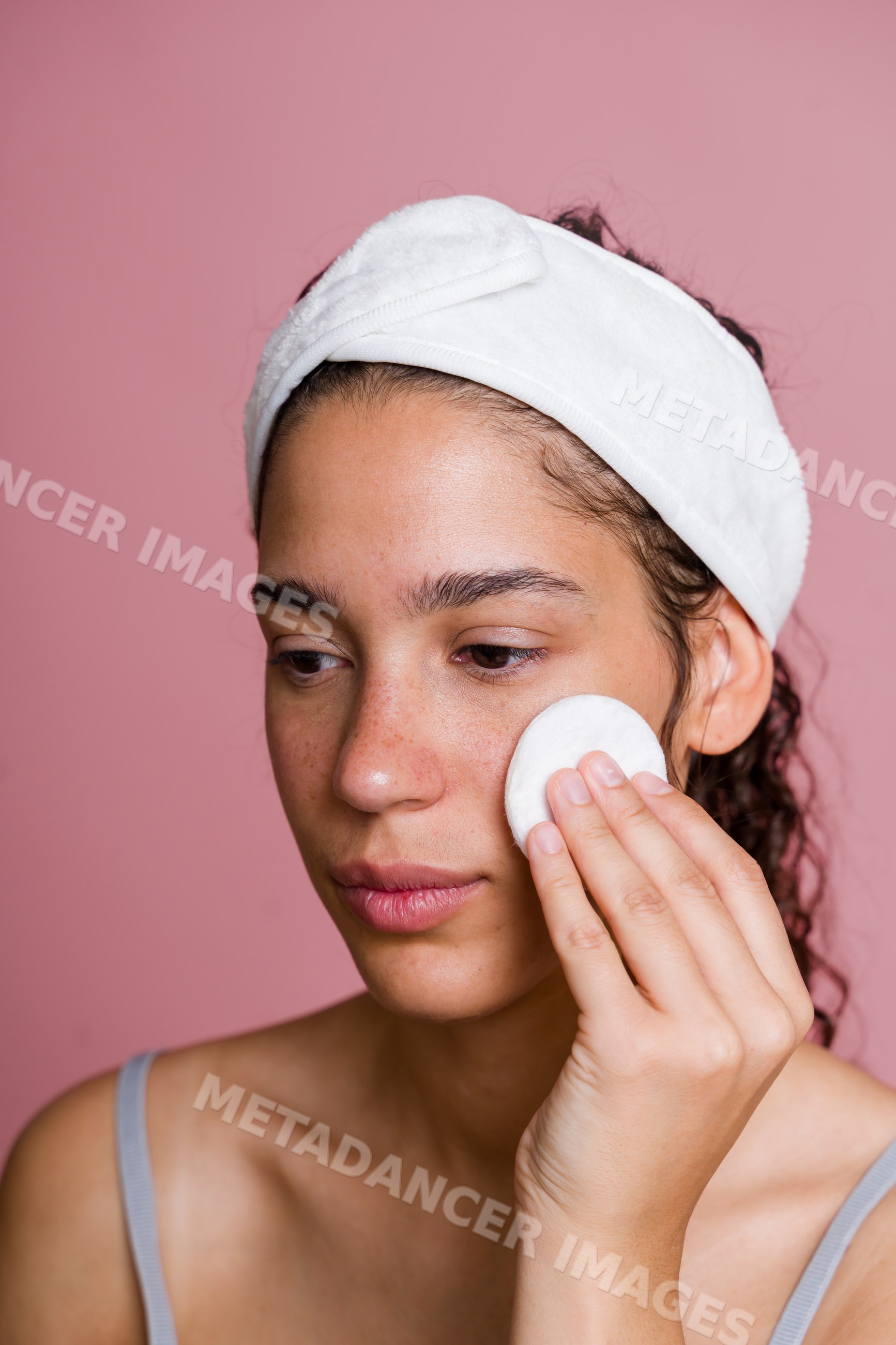 Hispanic woman applying skincare with a cotton pad and white headband