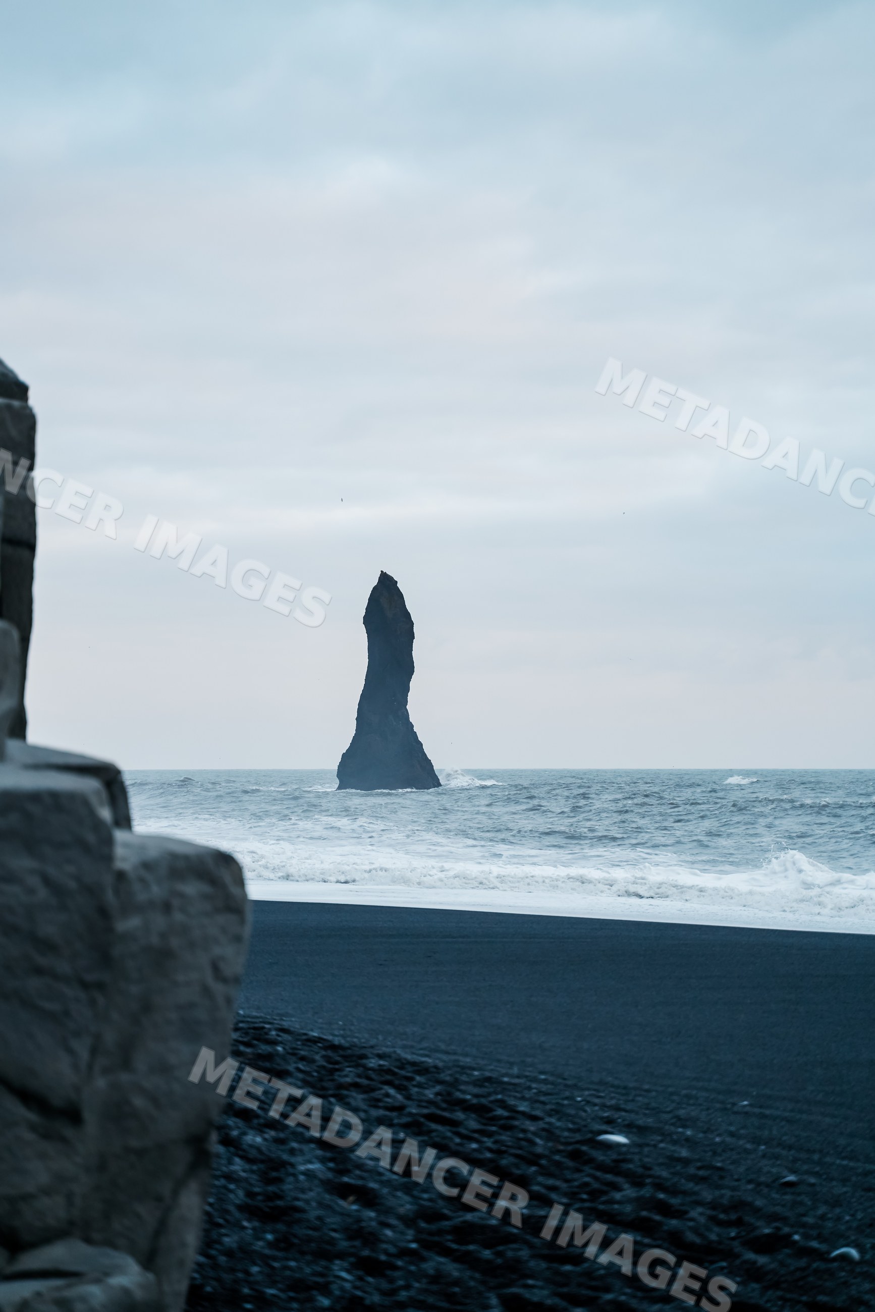 A tall sea stack rises from the ocean at a black sand beach in a beach