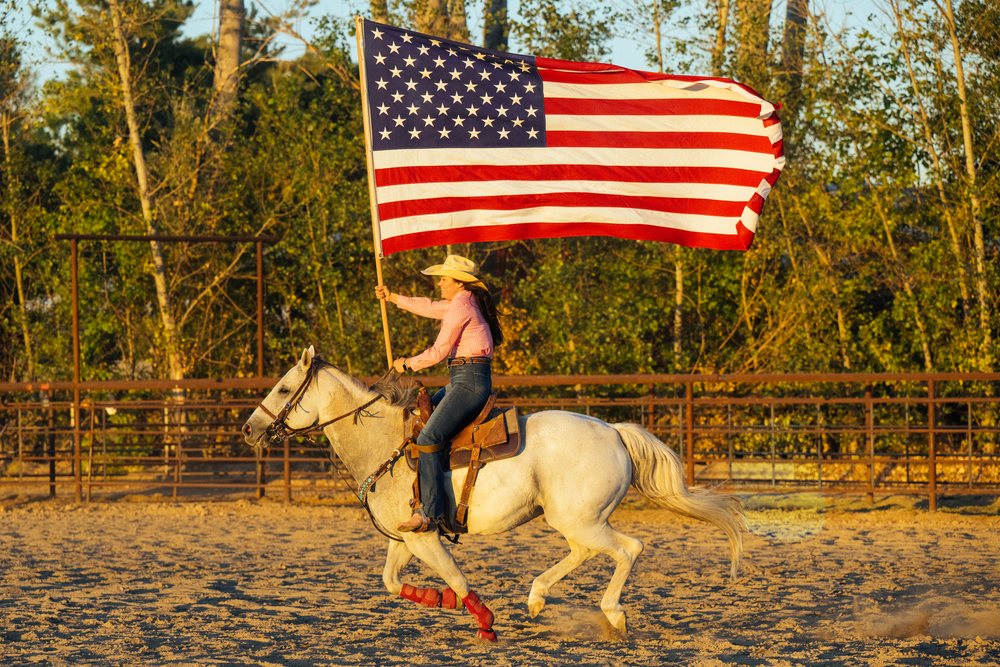 White woman riding horse carrying american flag