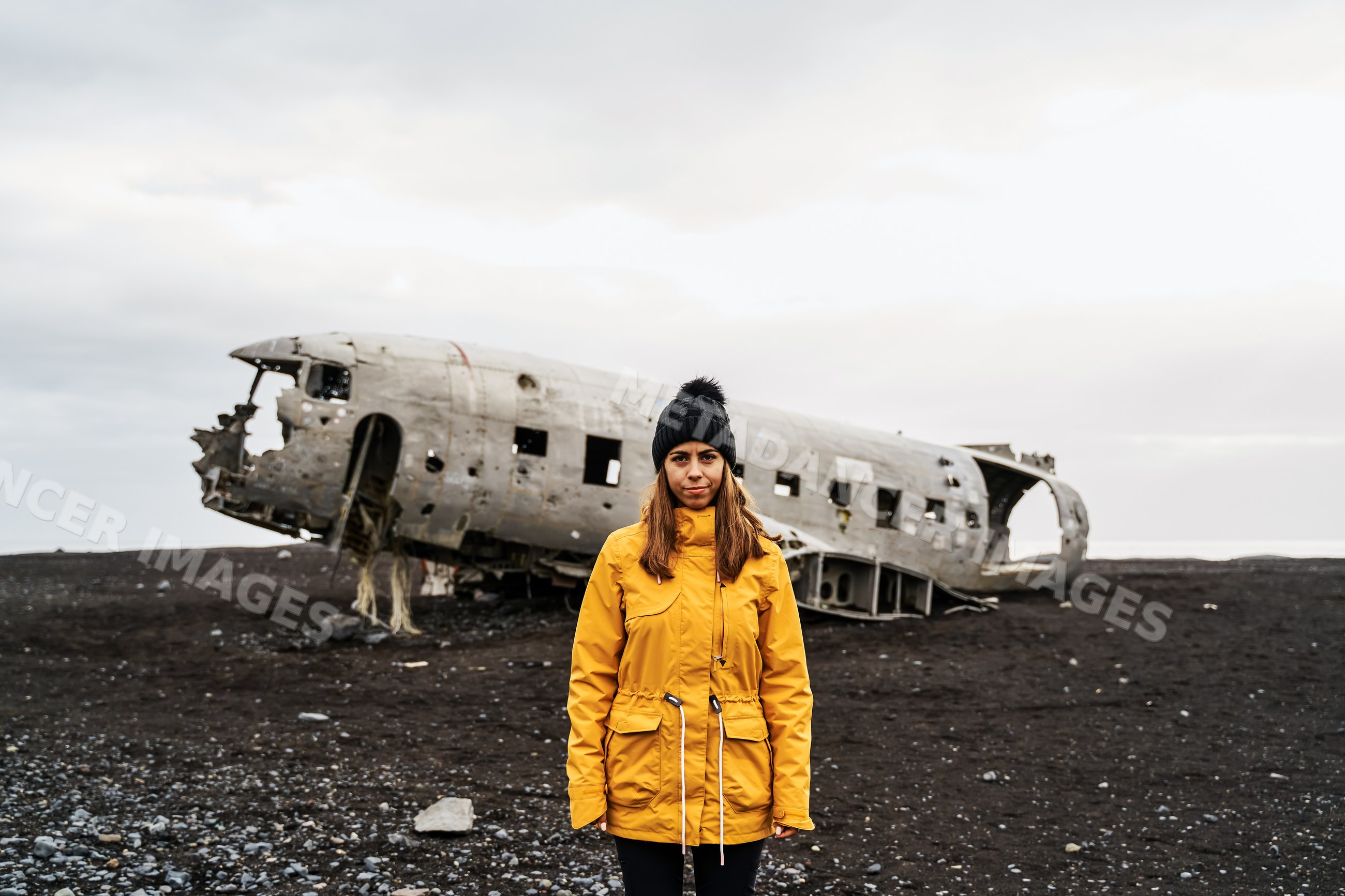 A white woman stands near a crashed airplane wreckage in Iceland's