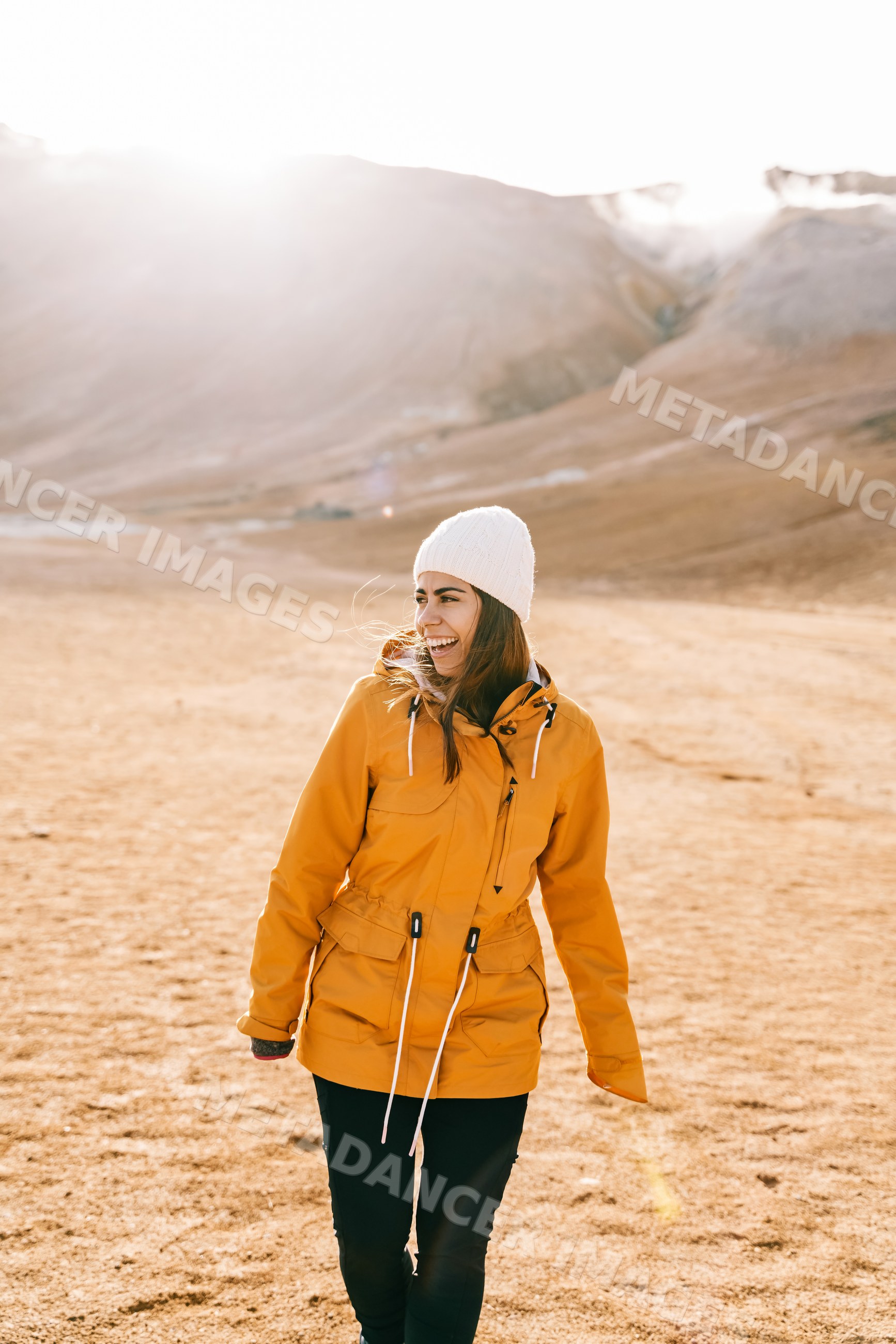 A white woman walks smiling in a yellow jacket on a mountain