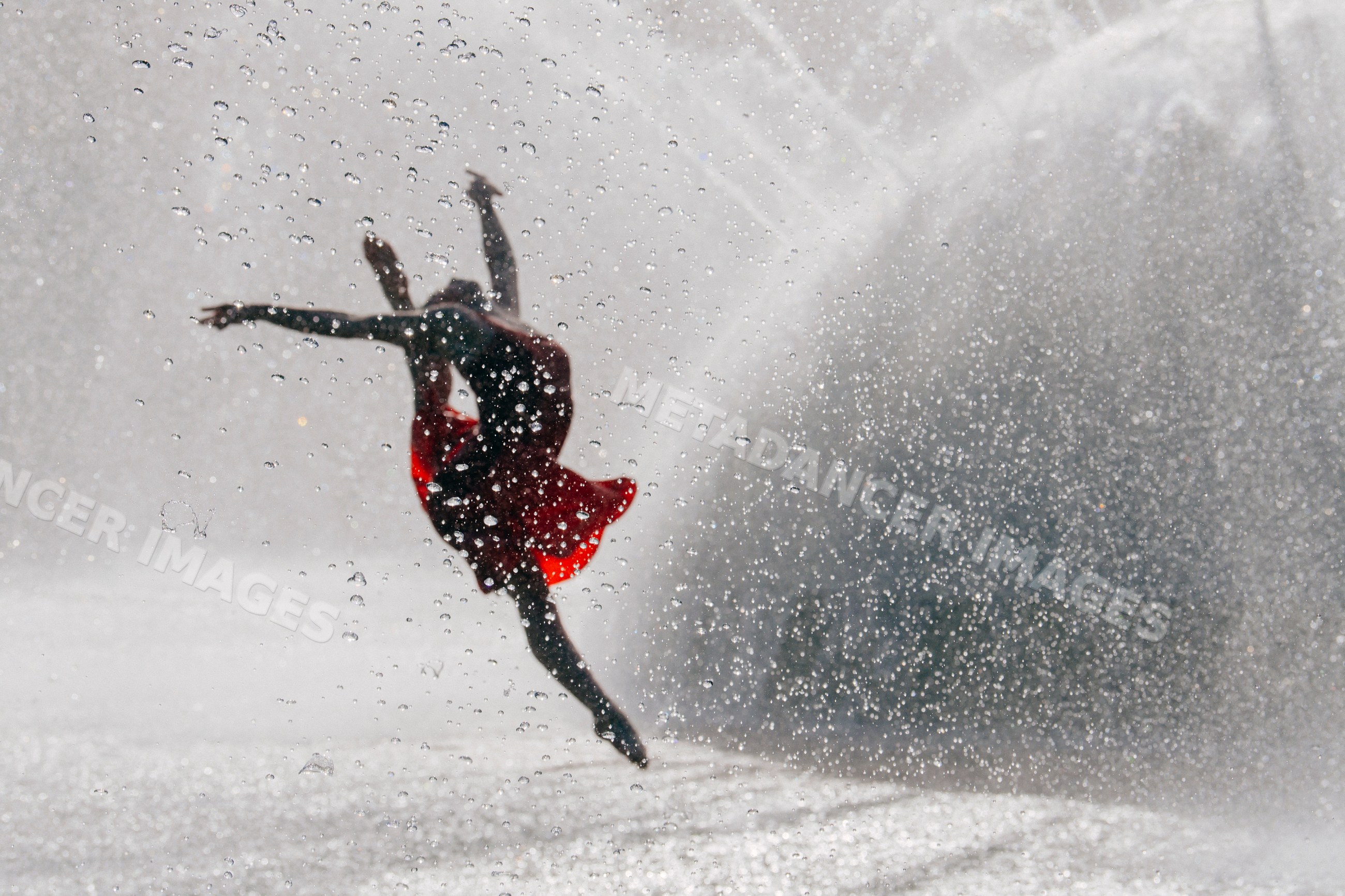 White dancer leaping through water droplets in a red dress outdoors