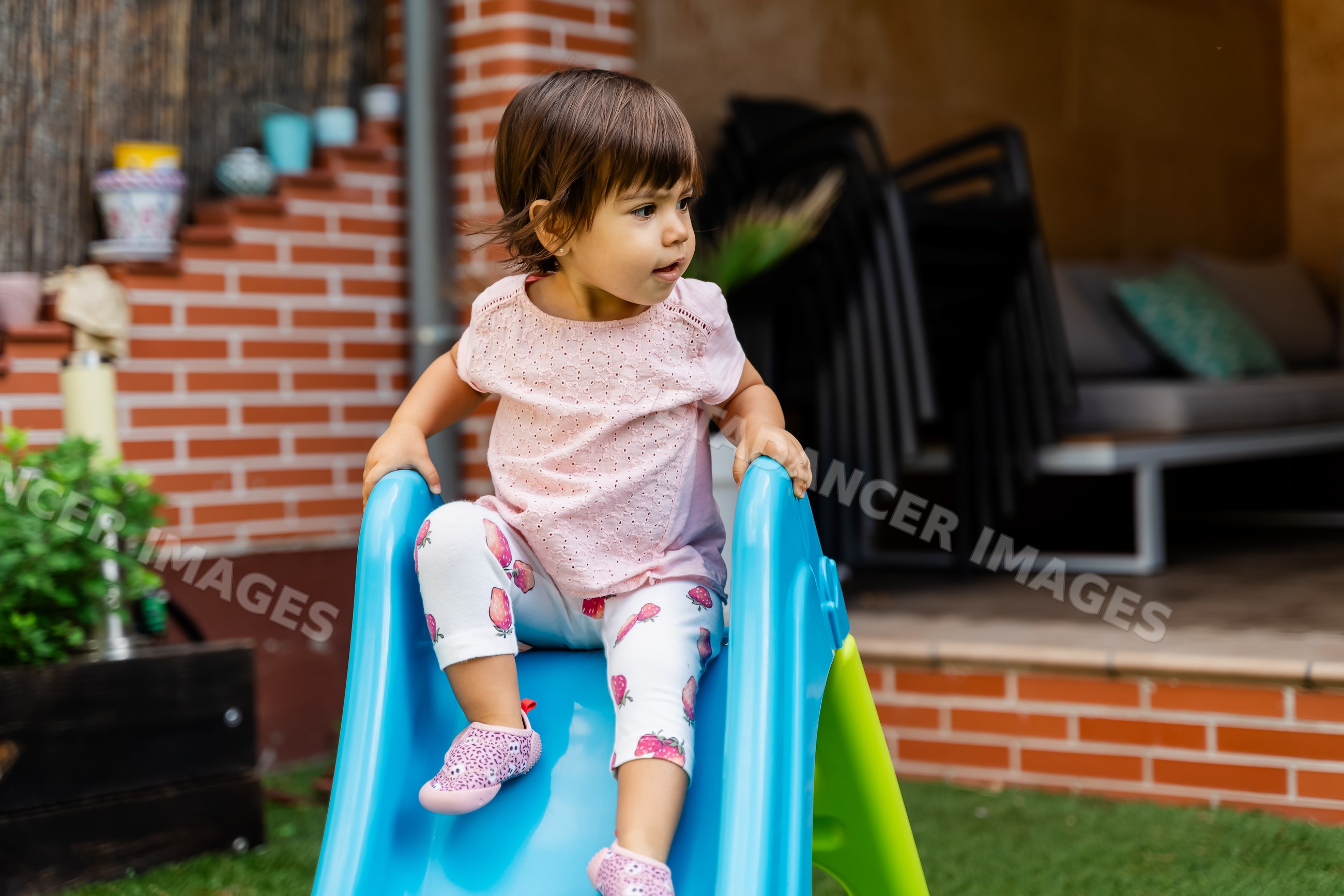 Toddler white girl playing on blue slide in backyard playground