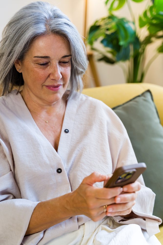 Middle-aged white woman sitting on yellow sofa using smartphone