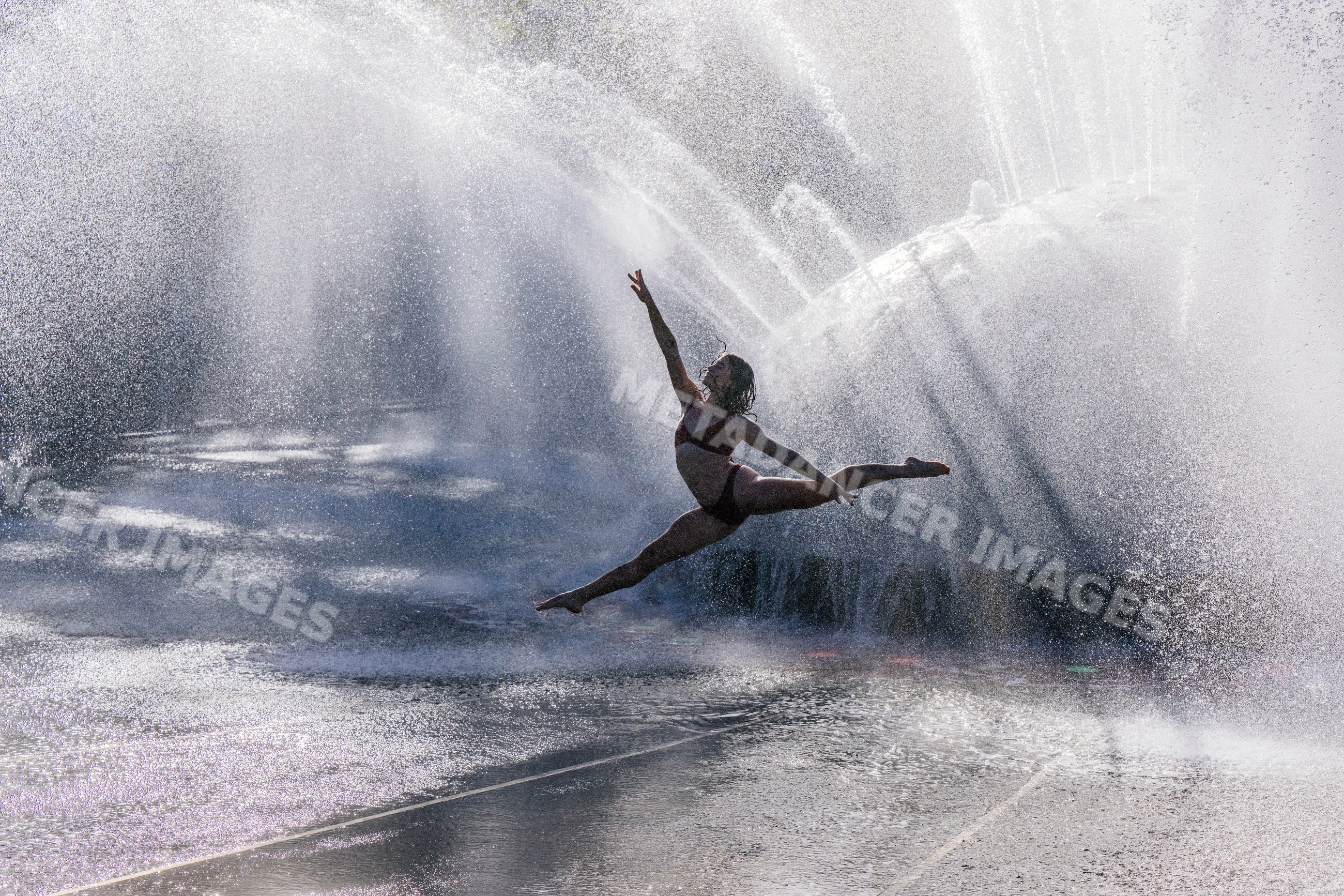 White woman performing a graceful dance leap through water fountain