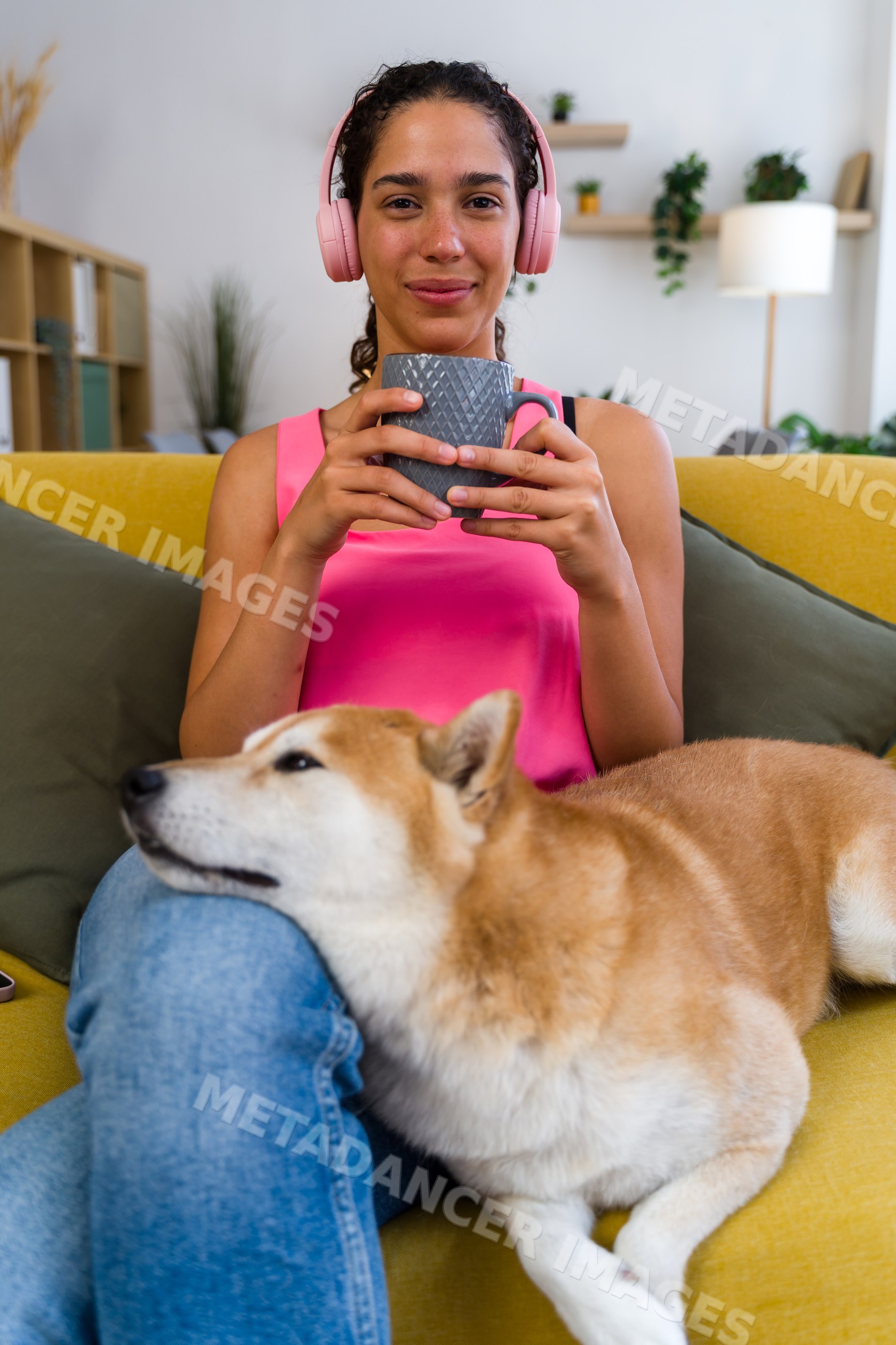 A Hispanic woman relaxes on a sofa with her dog and drinks from a mug