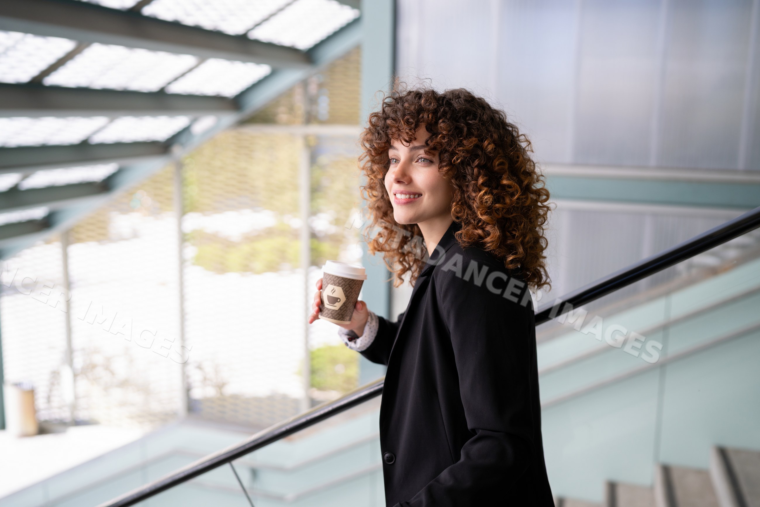 White woman with curly hair holding coffee on modern staircase