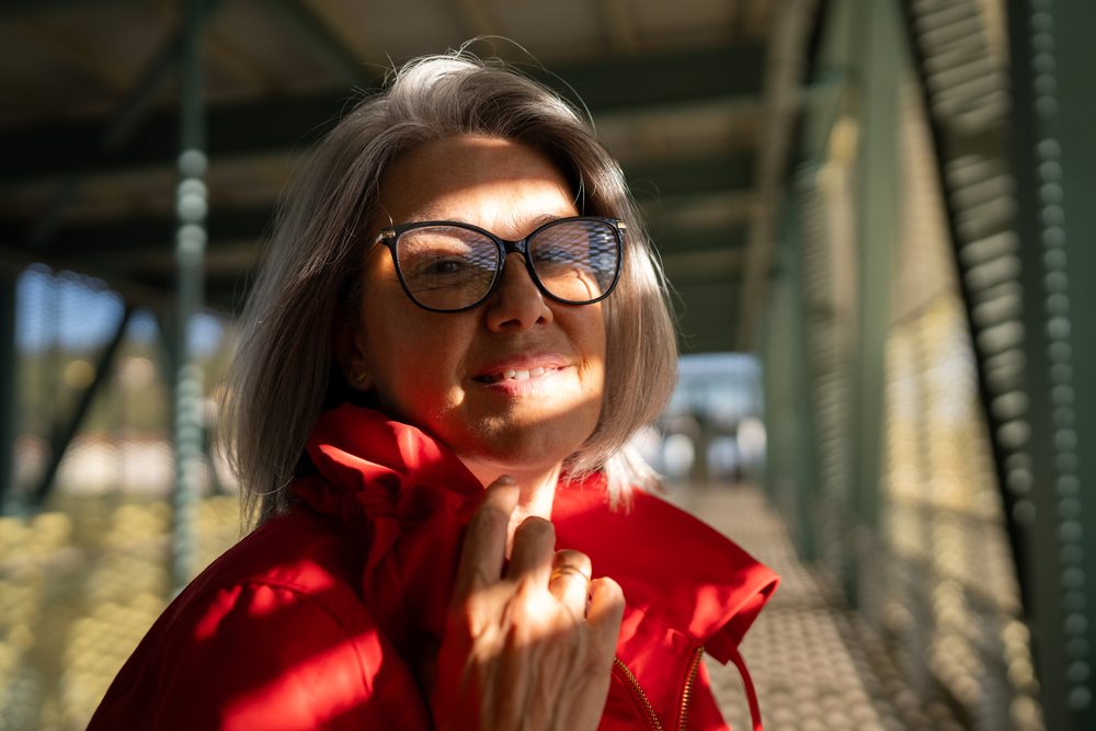 White woman smiling outdoors under patterned sunlight on metal bridge