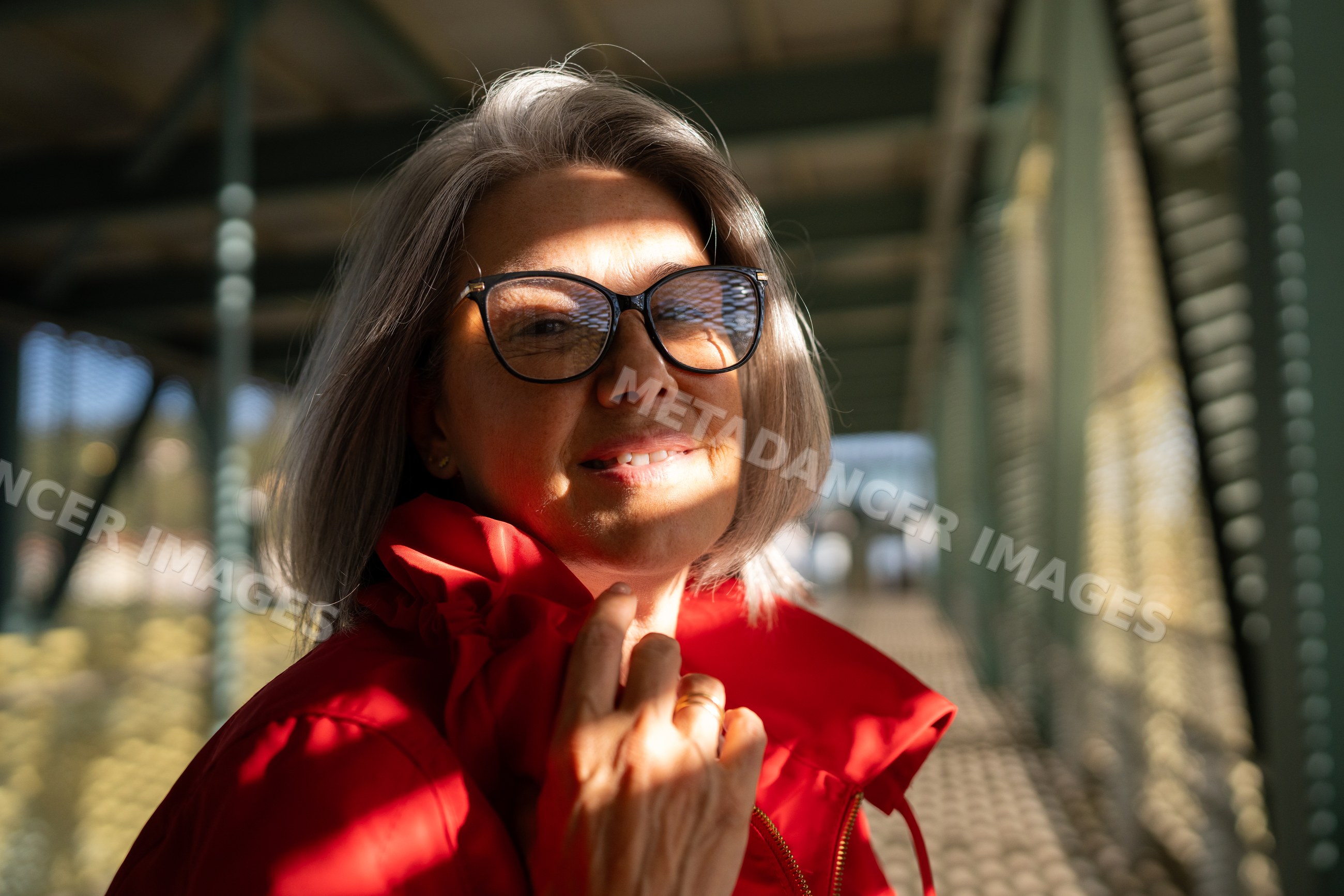 White woman smiling outdoors under patterned sunlight on metal bridge