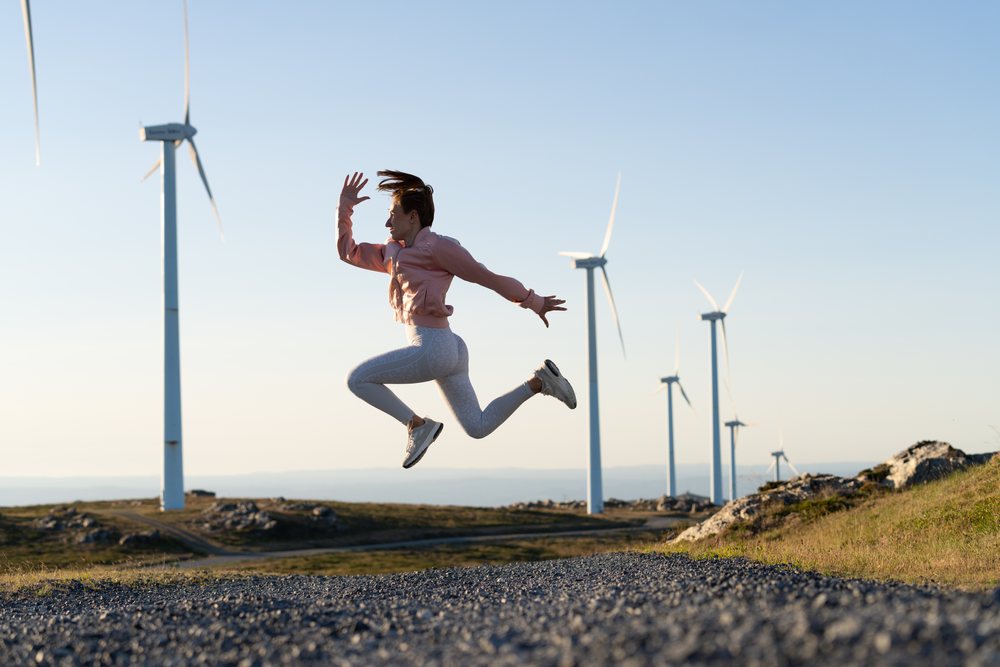 A white woman jumps actively near wind turbines in Galicia Spain