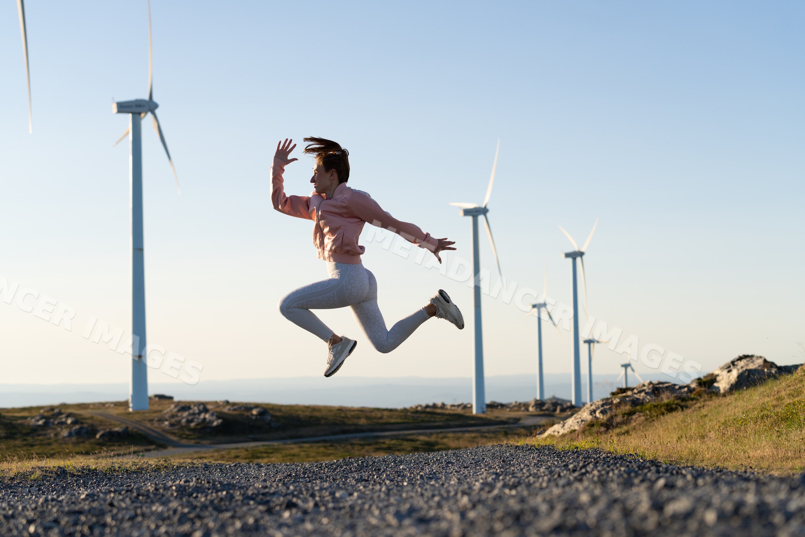 A white woman jumps actively near wind turbines in Galicia Spain