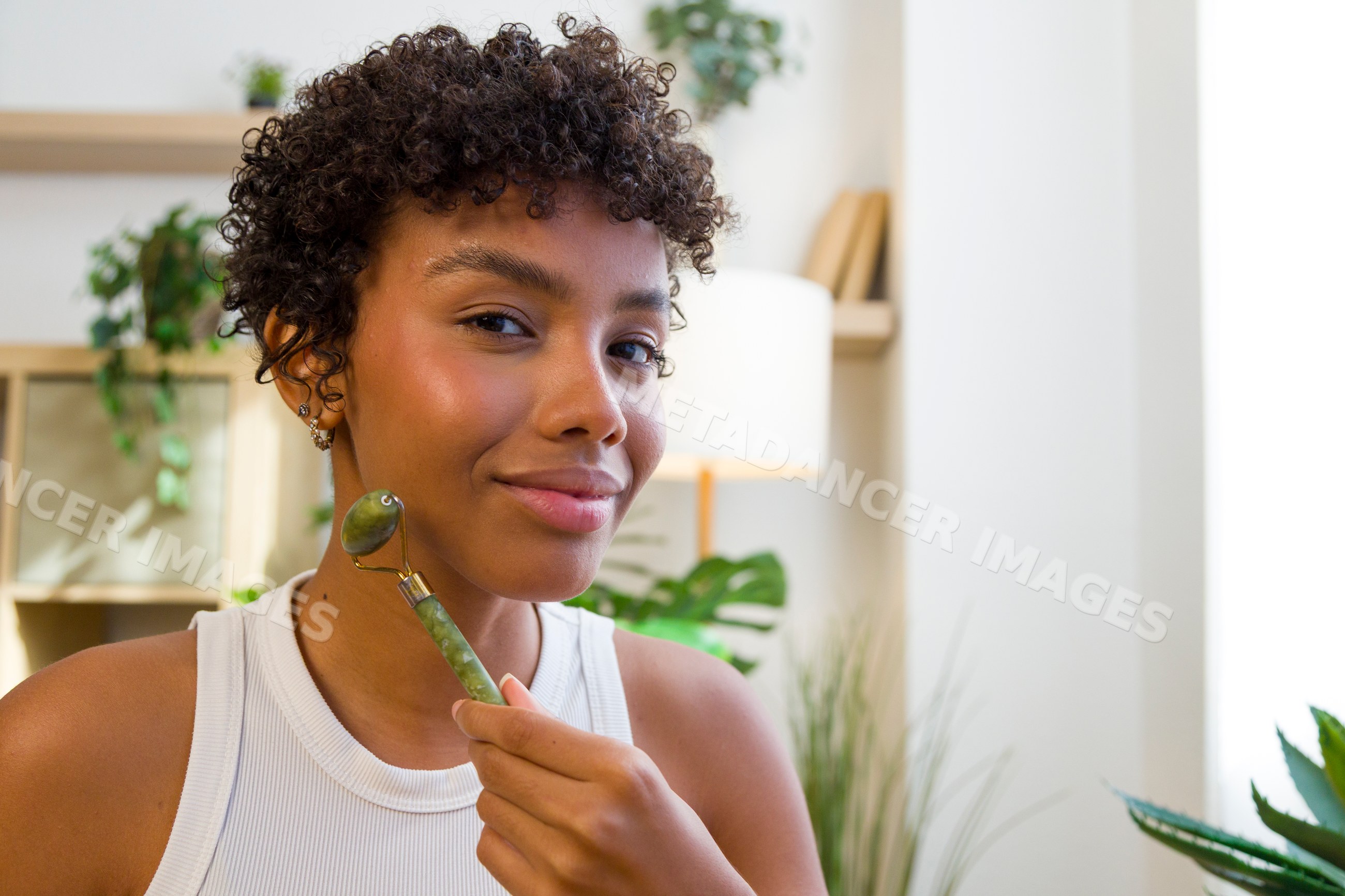 Young African American woman using jade roller for facial massage
