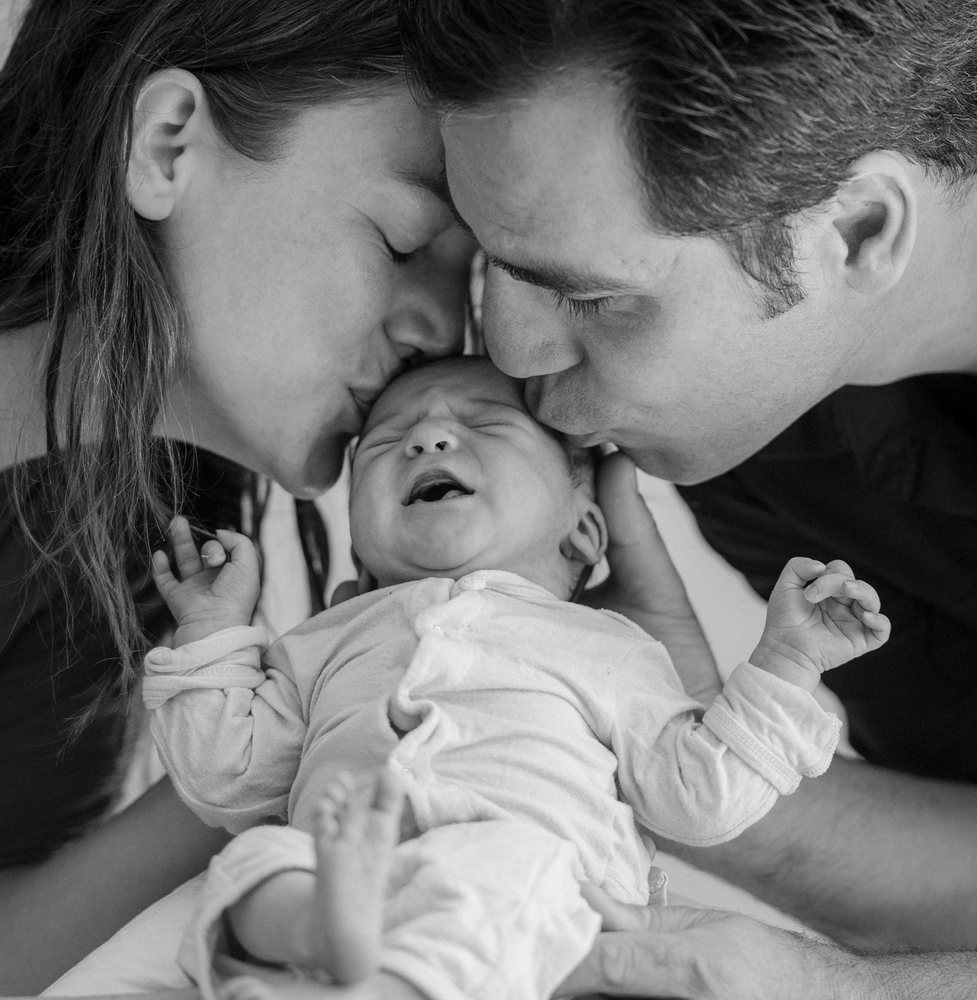 Newborn baby kissed by parents in loving family moment